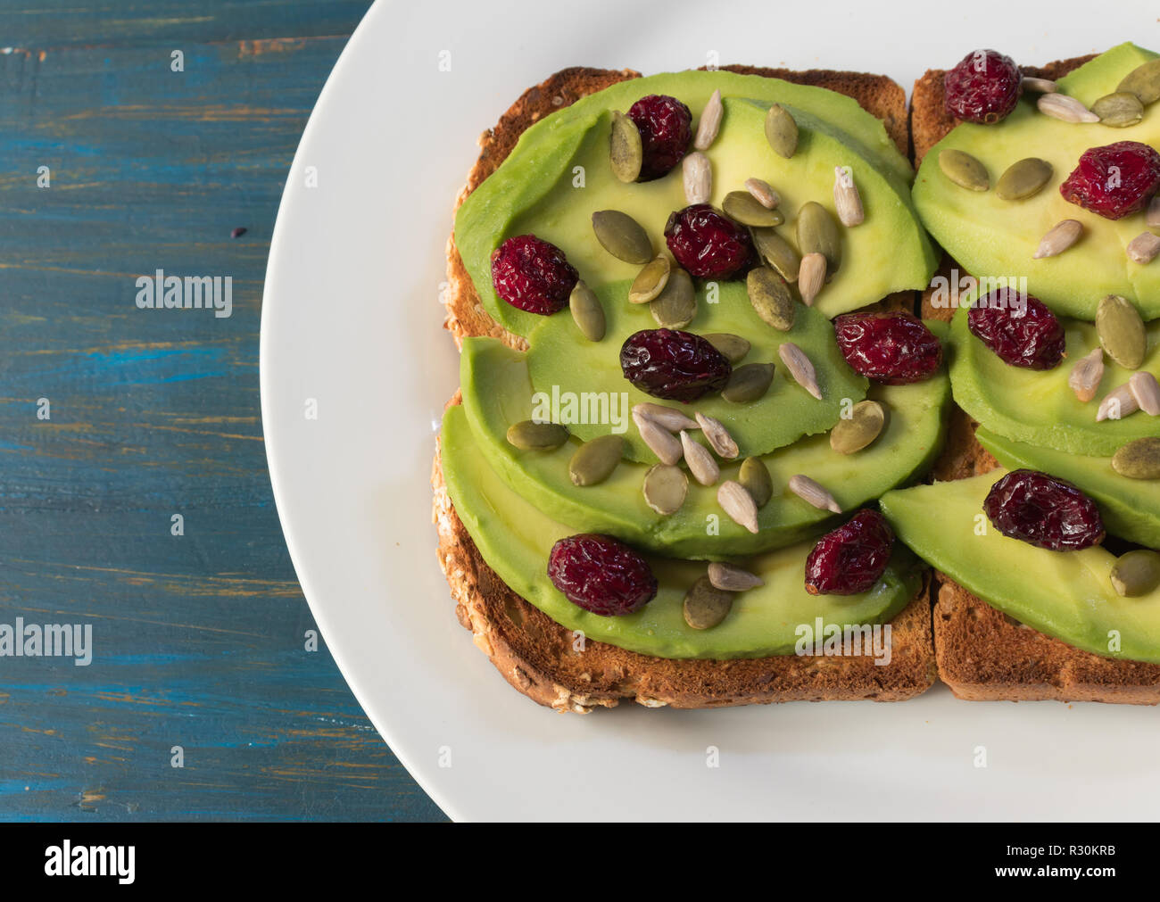 Vegetarian avocado toast with red cranberries, pumpkin seeds and sunflower seeds on a white plate Stock Photo
