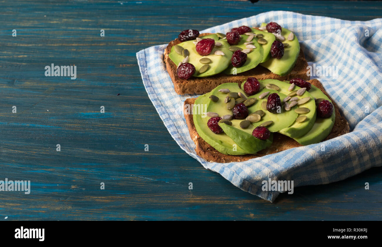 Vegetarian avocado toast with red cranberries and pumpkin seeds and sunflower seeds on a kitchen towel on a blue wooden background Stock Photo