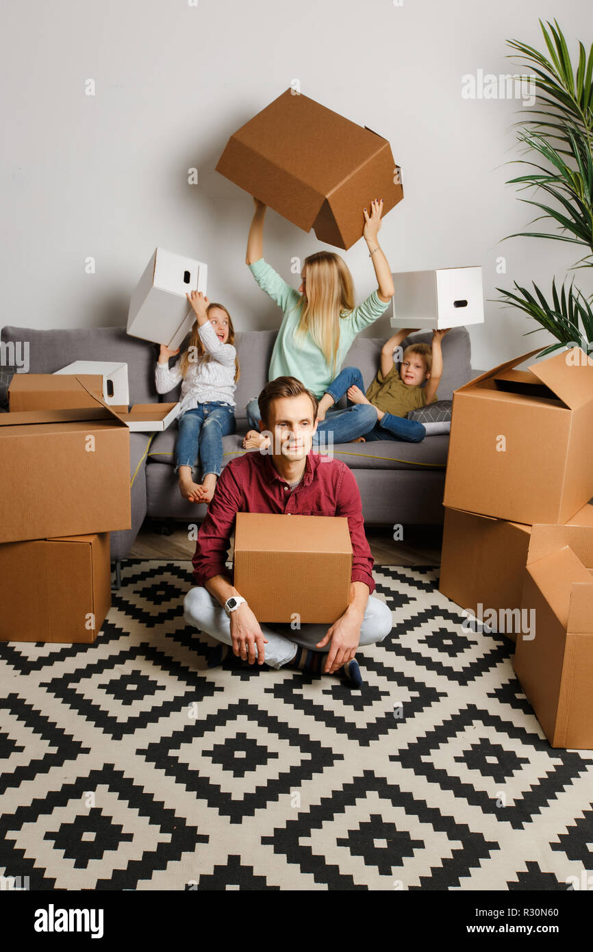 Photo of man sitting on floor among cardboard boxes and woman with son ...