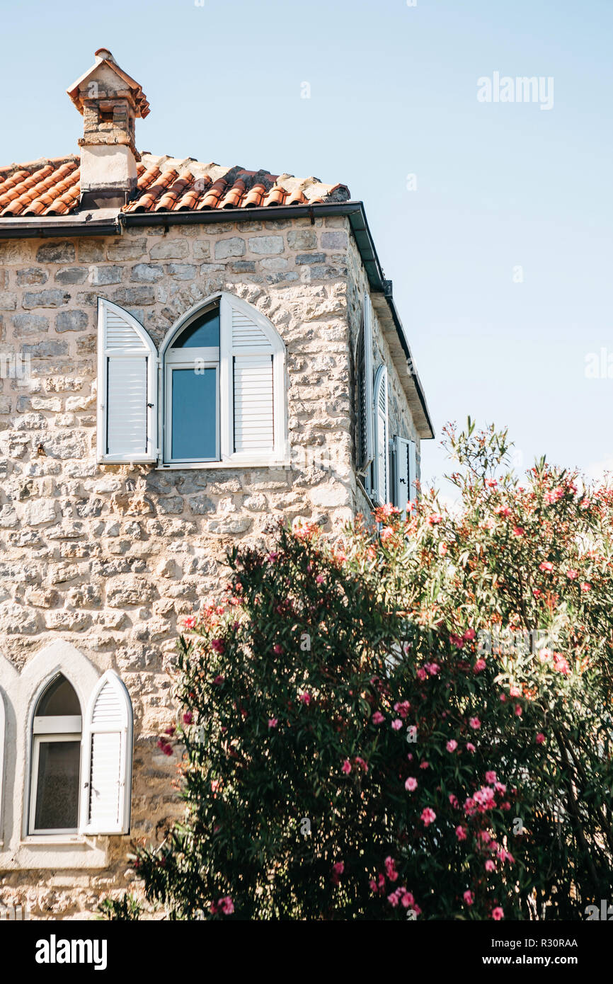 The facade of an ordinary old building with windows in Montenegro. Traditional housing. Near the garden with flowering trees. Stock Photo