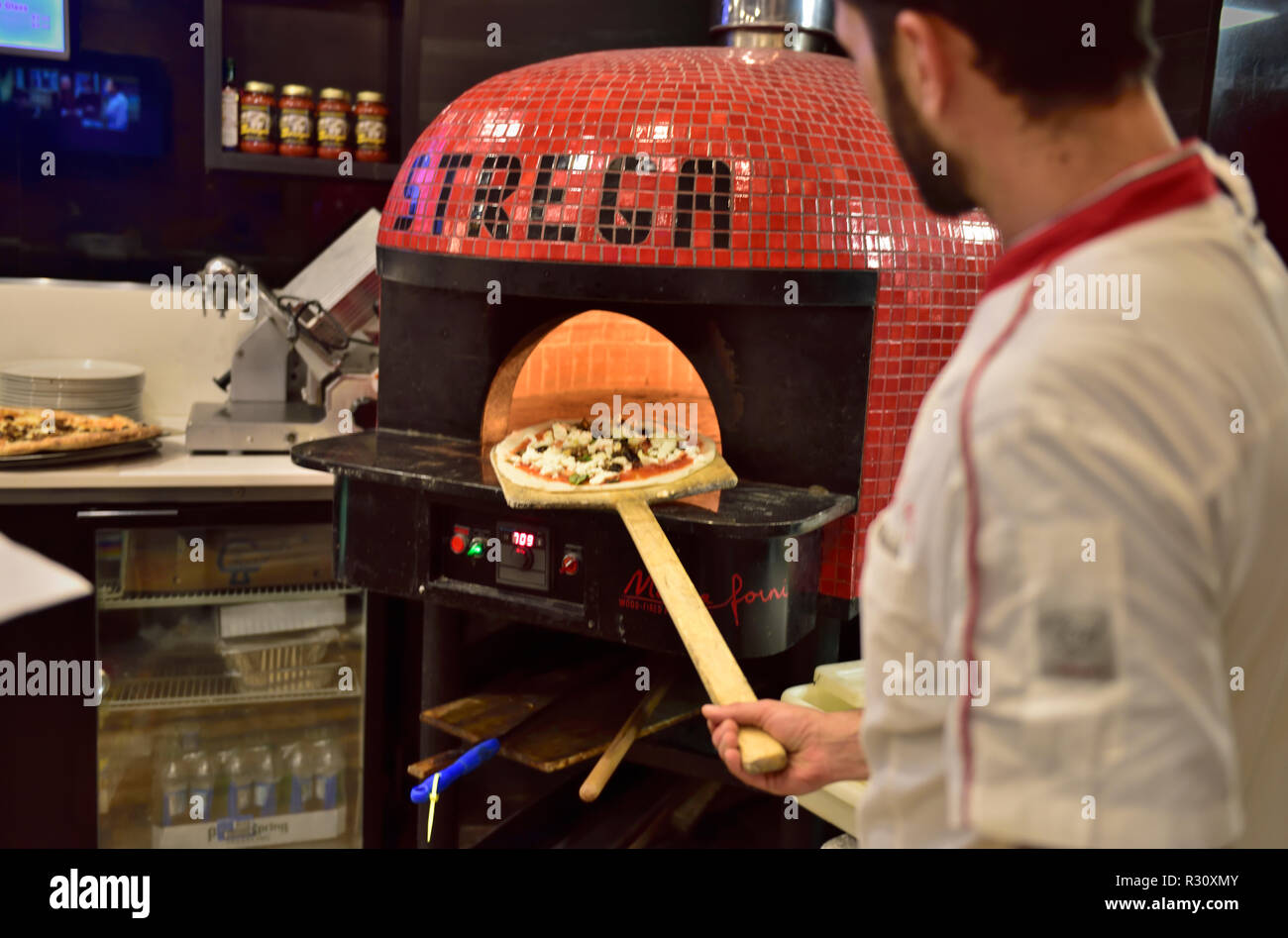 Pizza kitchen with chefs putting pizza into oven on long paddle, USA Stock Photo