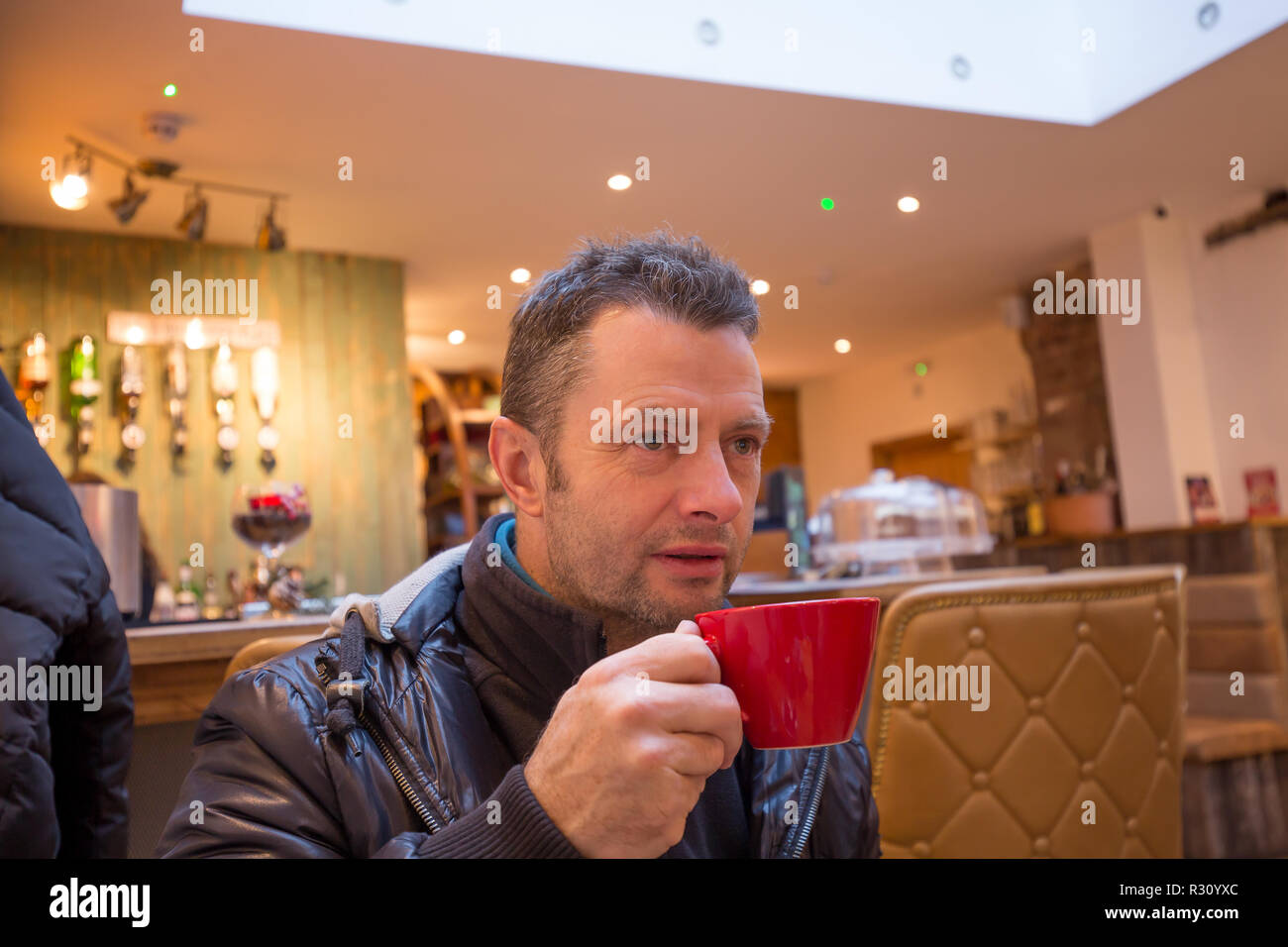 Close up of attractive caucasian male, in his forties, inside trendy bar enjoying a coffee from red cup he is holding. Stock Photo