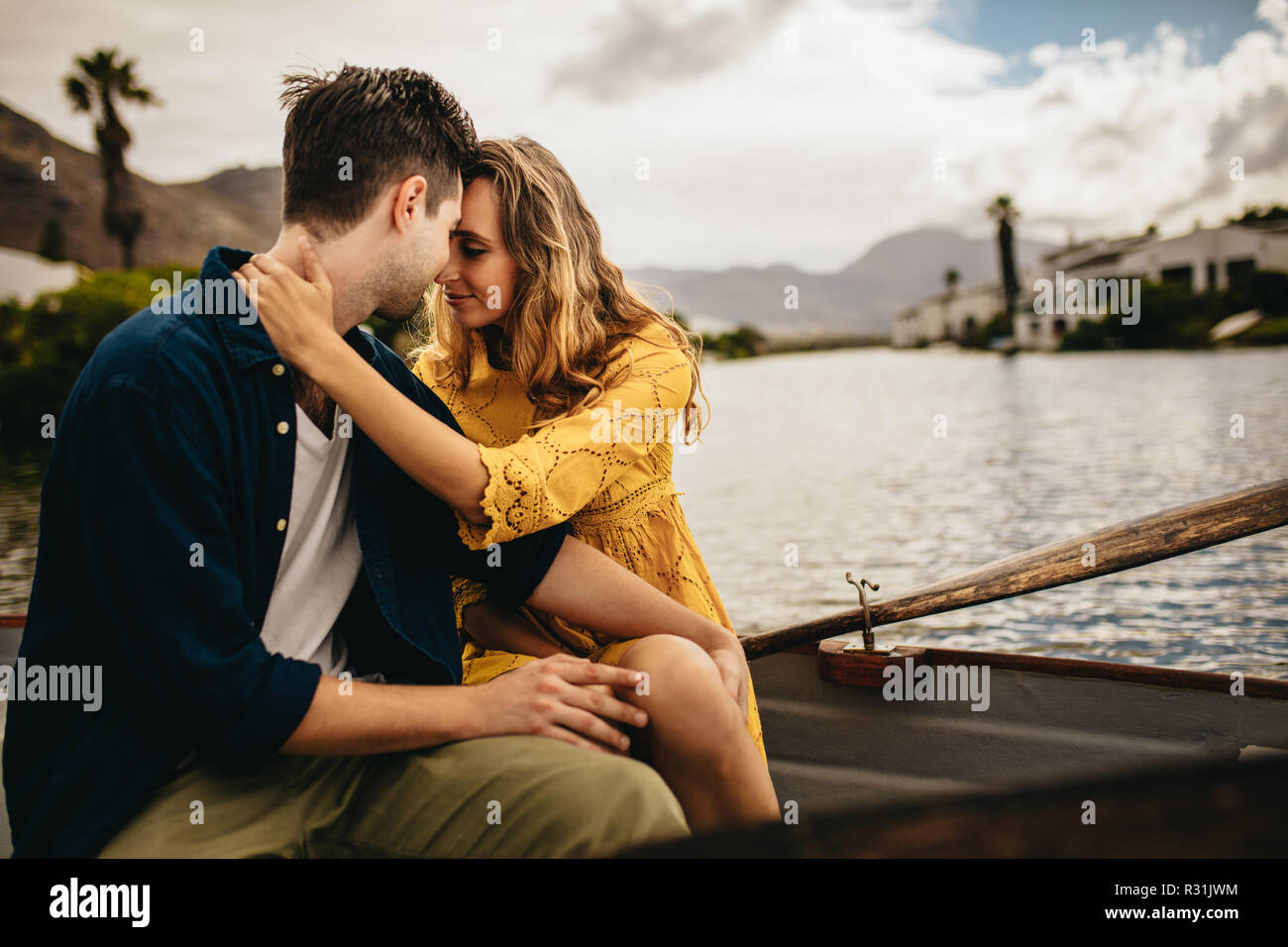 Couple in love sitting together in a boat holding each other. Woman holding her boyfriend touching their heads sitting in a boat during a date. Stock Photo