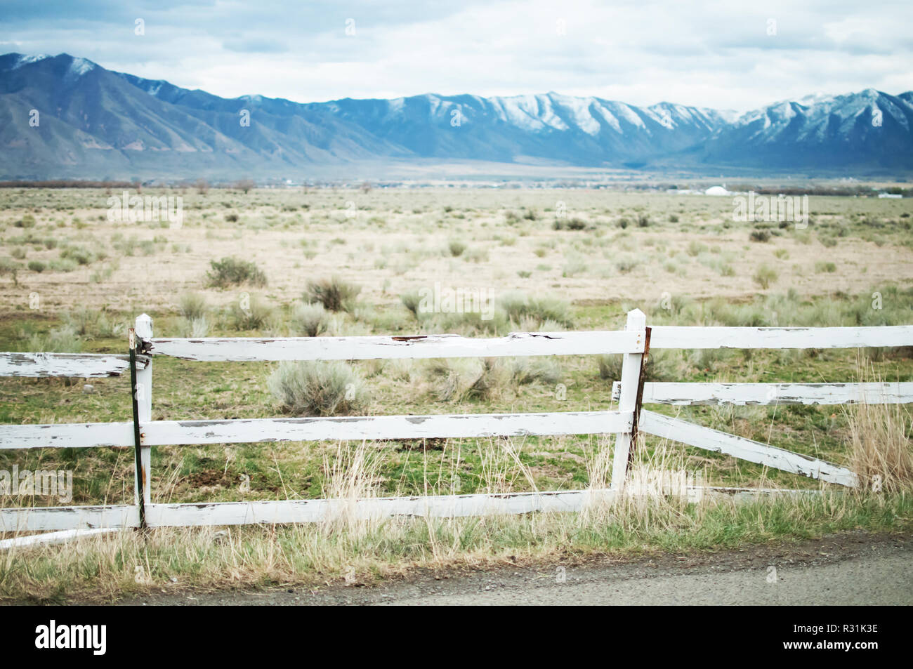 A broken white picket fence in front of open desert plain with mountains behind it in Utah. Stock Photo