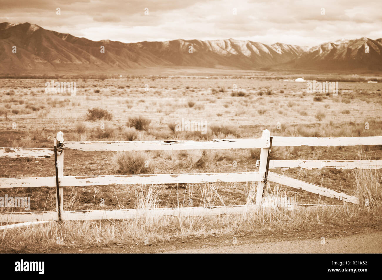 A broken white picket fence in front of open desert plain with mountains behind it in Utah in sepia. Stock Photo