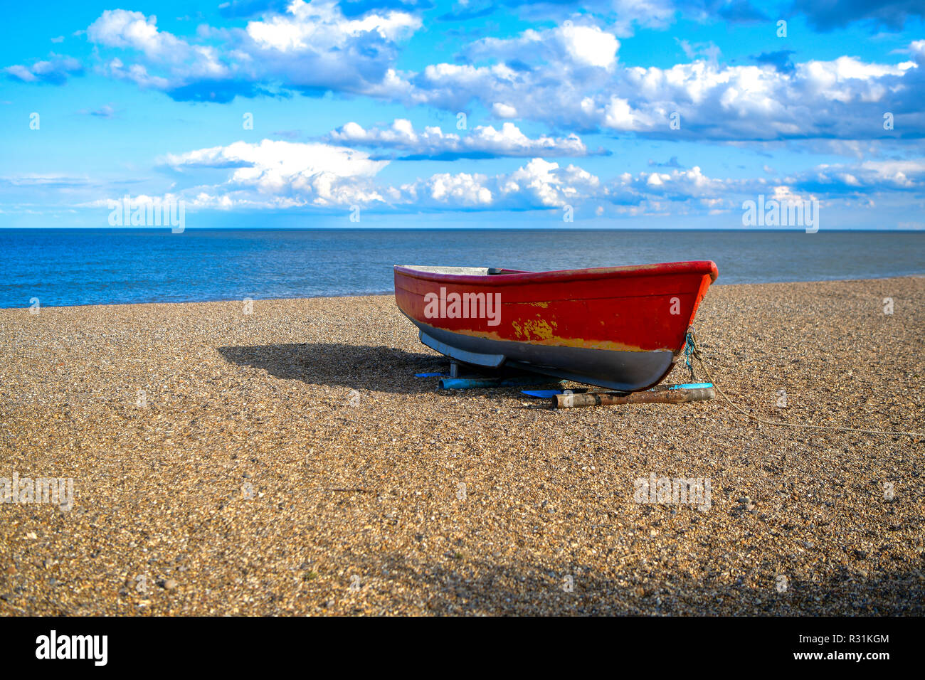 photo of a red-and-white boat on the sand, pebbles by the sea. UK Stock Photo