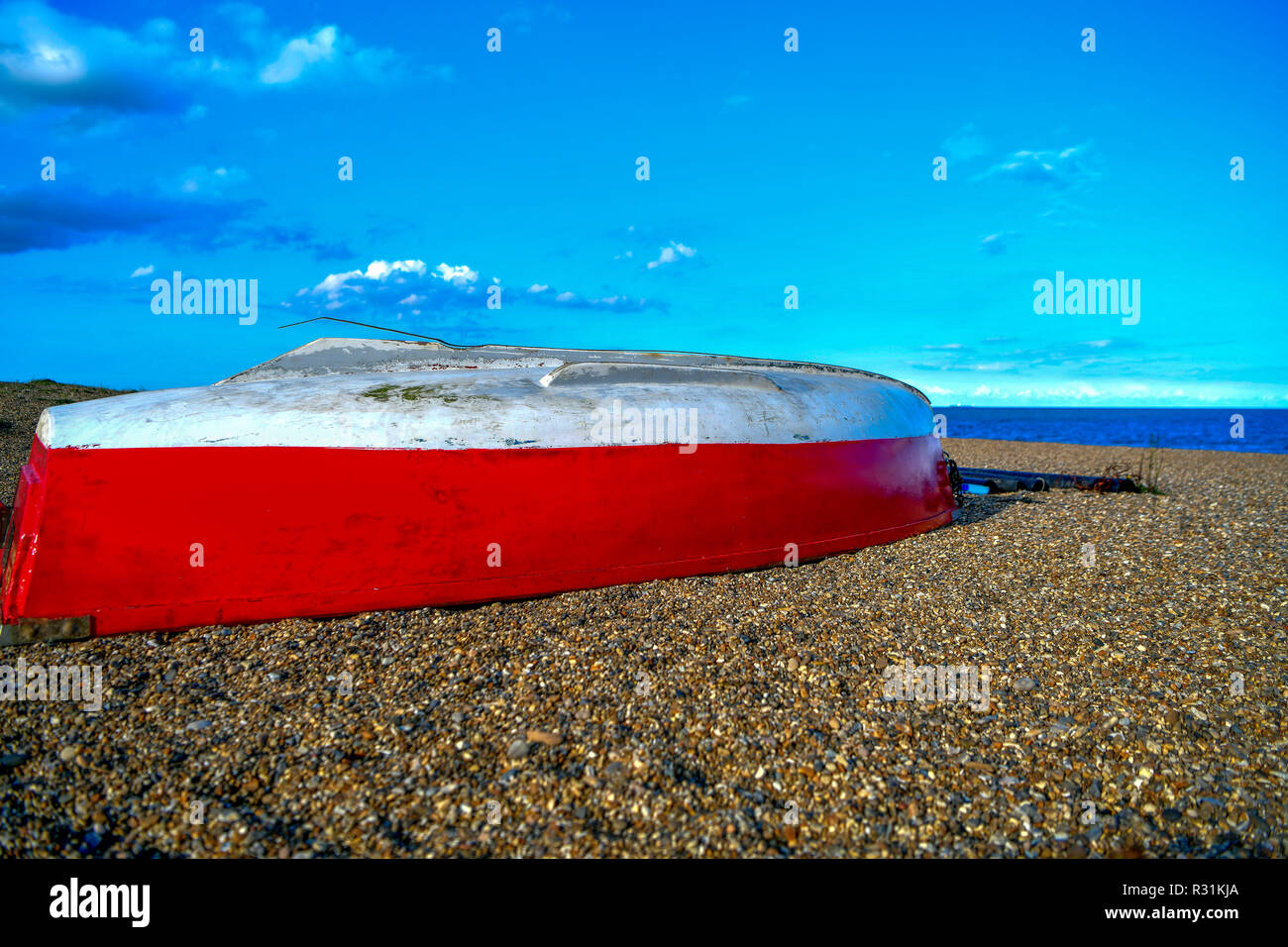 photo of a red-and-white boat on the sand, pebbles by the sea. UK Stock Photo