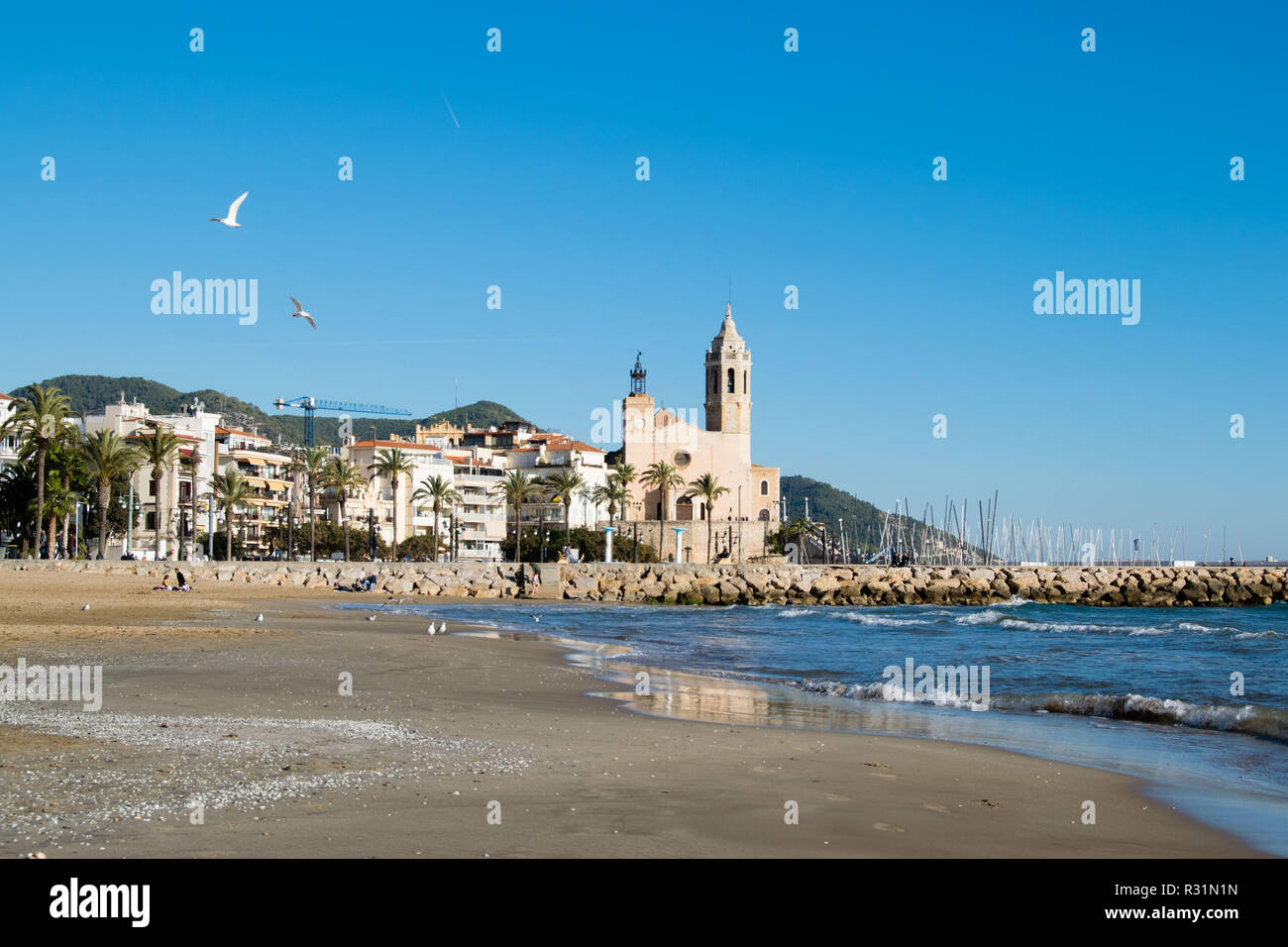 The beautiful town of Sitges with seagulls, winter Spain, Landscape of the coastline in Sitges, Parròquia de Sant Bartomeu i Santa Tecla Stock Photo