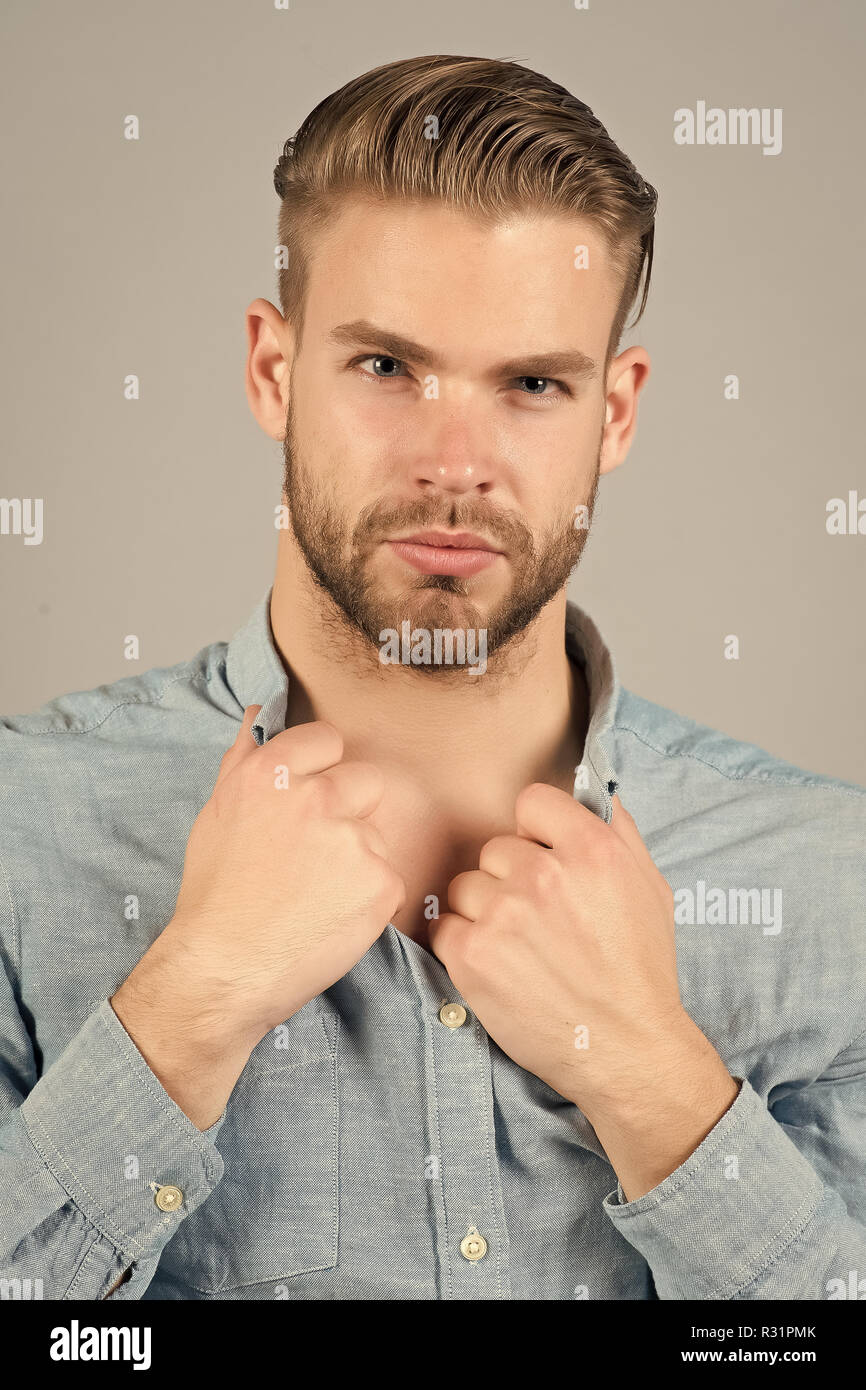Guy with bearded face, stylish hair, haircut hold blue shirt collar on grey  background. Grooming, male beauty concept Stock Photo - Alamy
