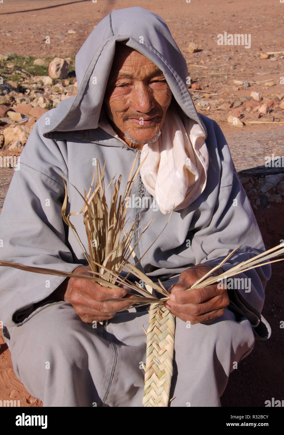 MARRAKESH, MOROCCO - 21,02,2012: A friendly old typically dressed Berber man crafts straps from straw in the foothills of the High Atlas Mountains. Stock Photo