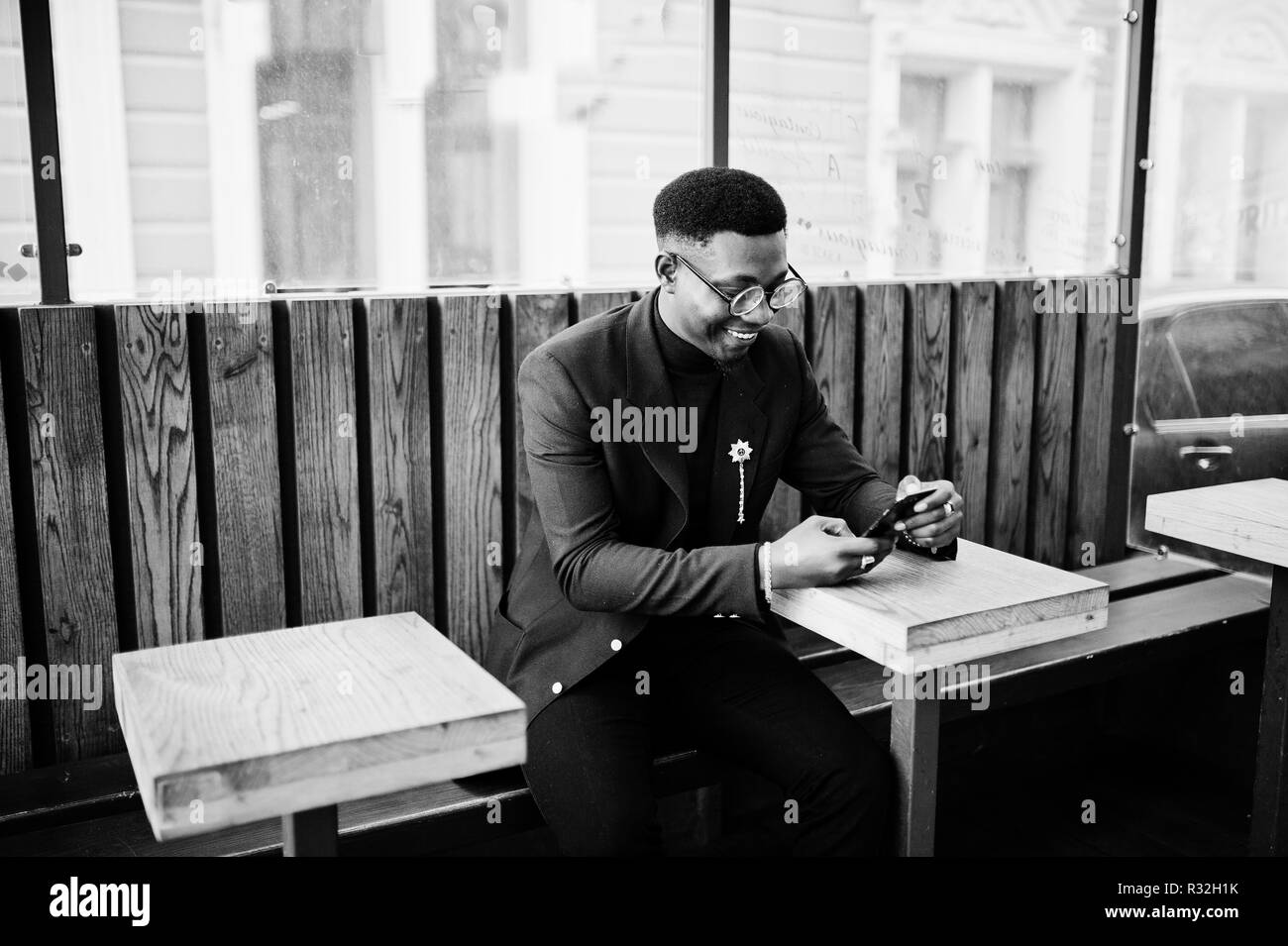 Amazingly looking african american man wear at blue blazer with brooch, black turtleneck and glasses posed at street. Fashionable black guy sitting be Stock Photo