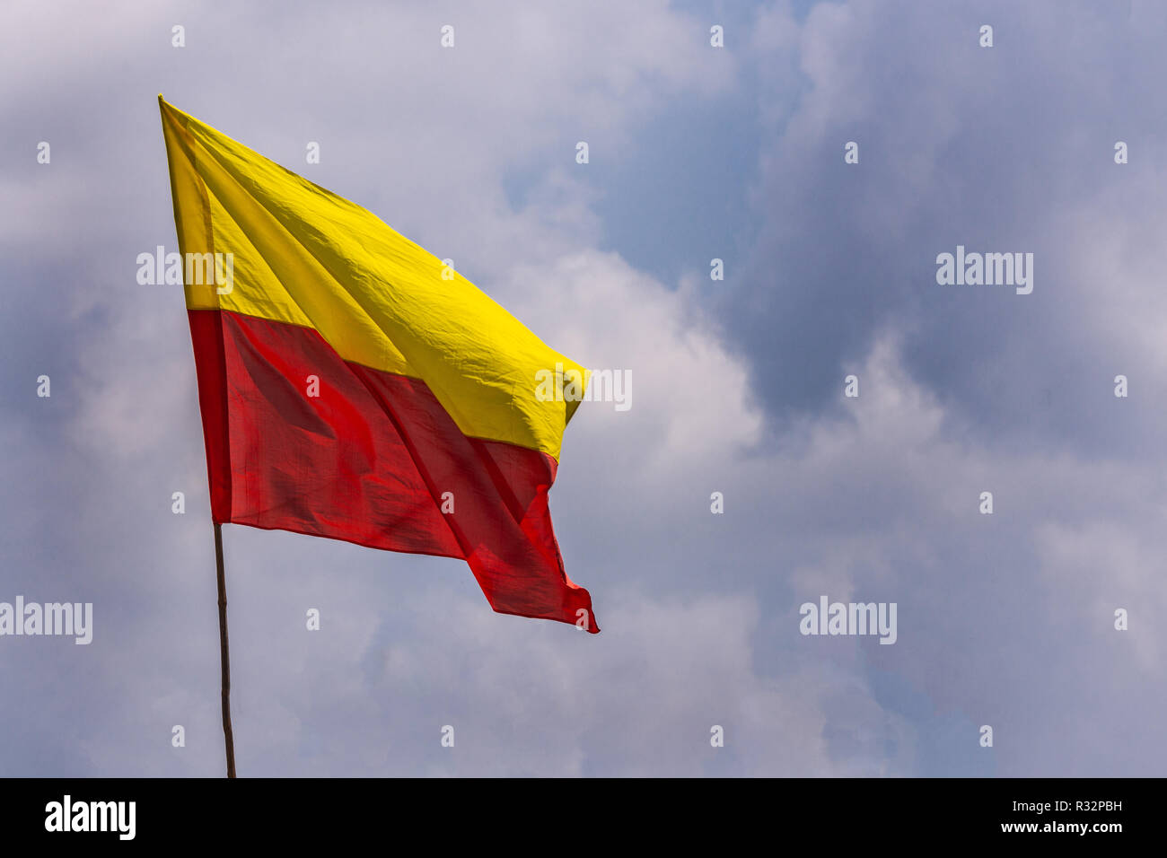 Belur, Karnataka, India - November 2, 2013: Yellow and red State flag on pole floats against blue sky with white clouds. Stock Photo