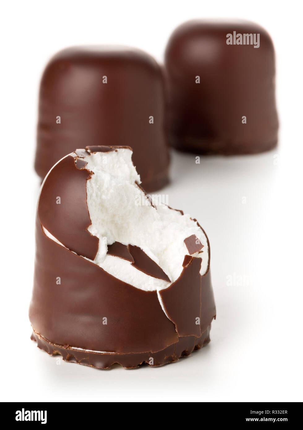 Whole and bitten off german specialty sweet 'Schokokuss' or 'Schokoschaumkuss' (small chocolate-covered cake filled with foamy sugar) over white backg Stock Photo