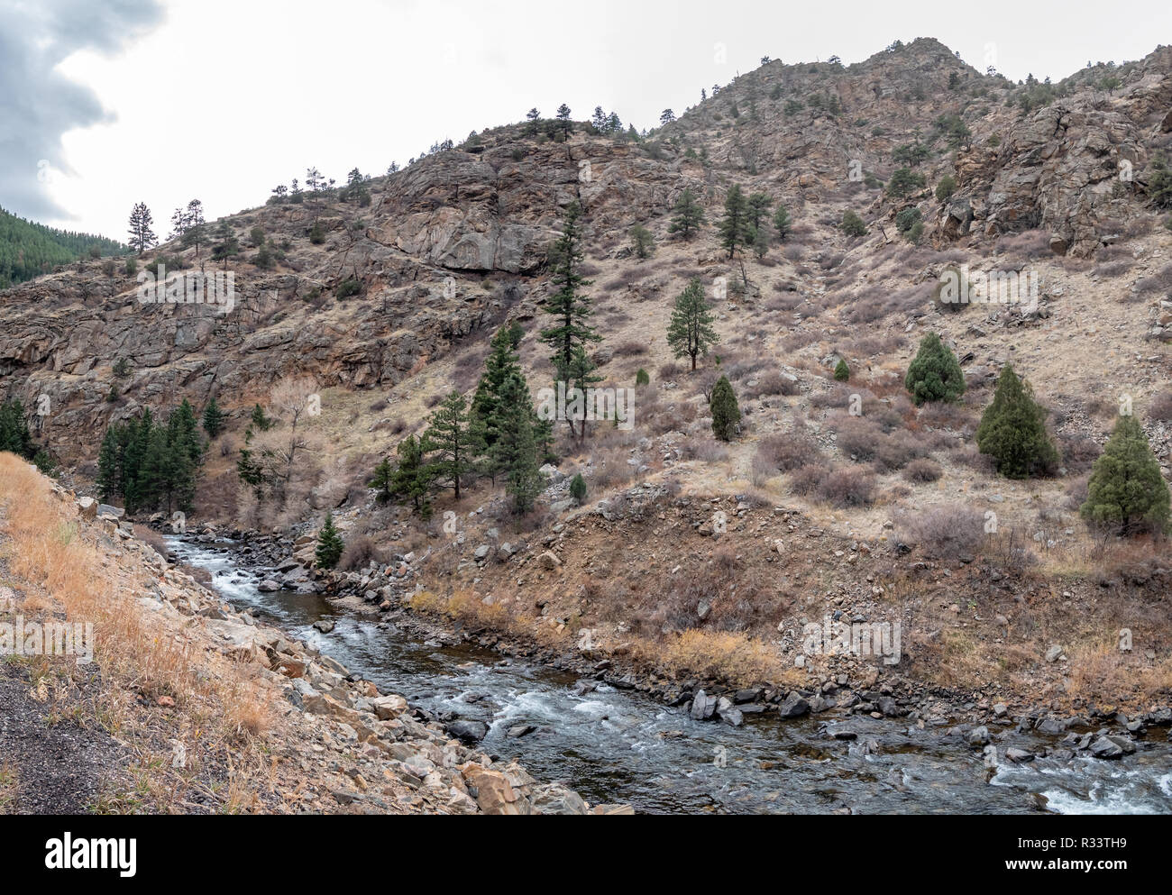 View of Mountain Stream Flowing Next to Tall Rocky Mountain Stock Photo