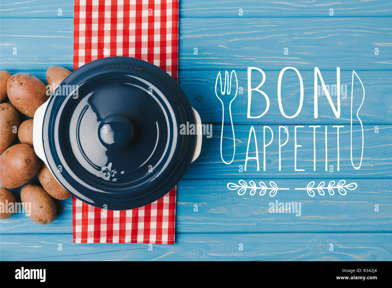 top view of pan and potatoes on blue table, bon appetit lettering Stock