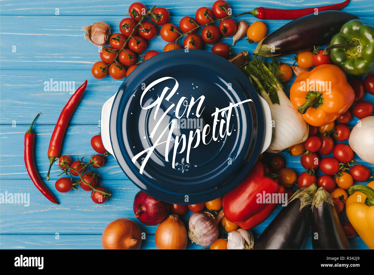 top view of pan between vegetables on blue table, bon appetit lettering