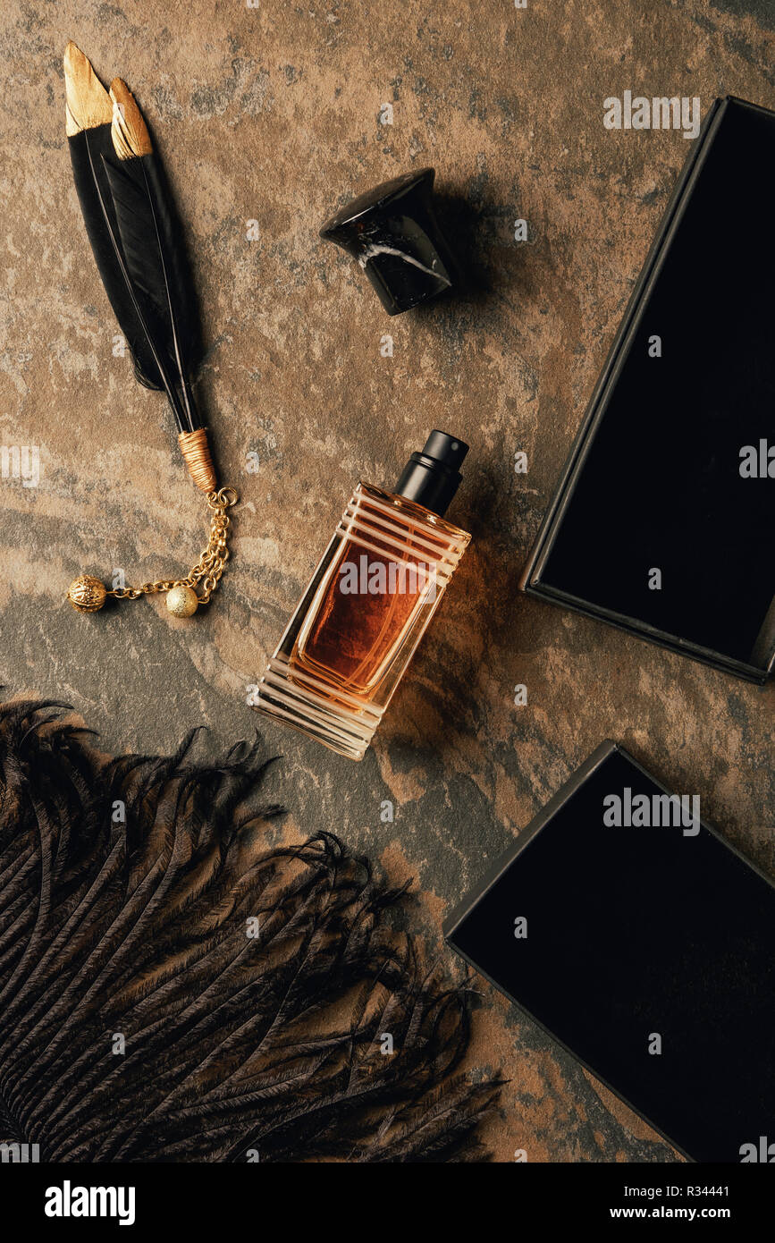 top view of perfume and decorative black feathers on brown weathered surface Stock Photo