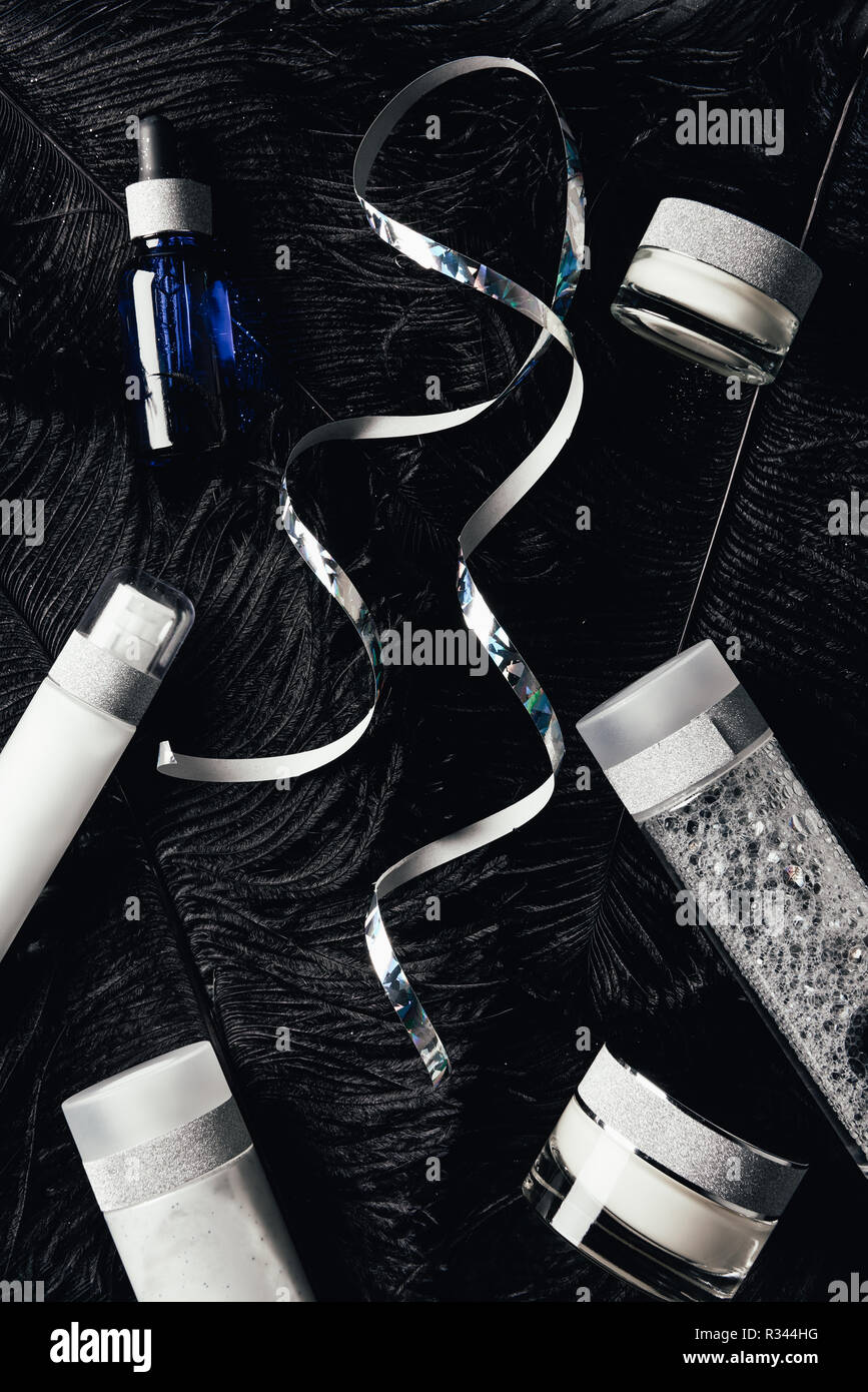 view from above of ribbon, serum, micellar water, beauty cream on surface with black feathers Stock Photo