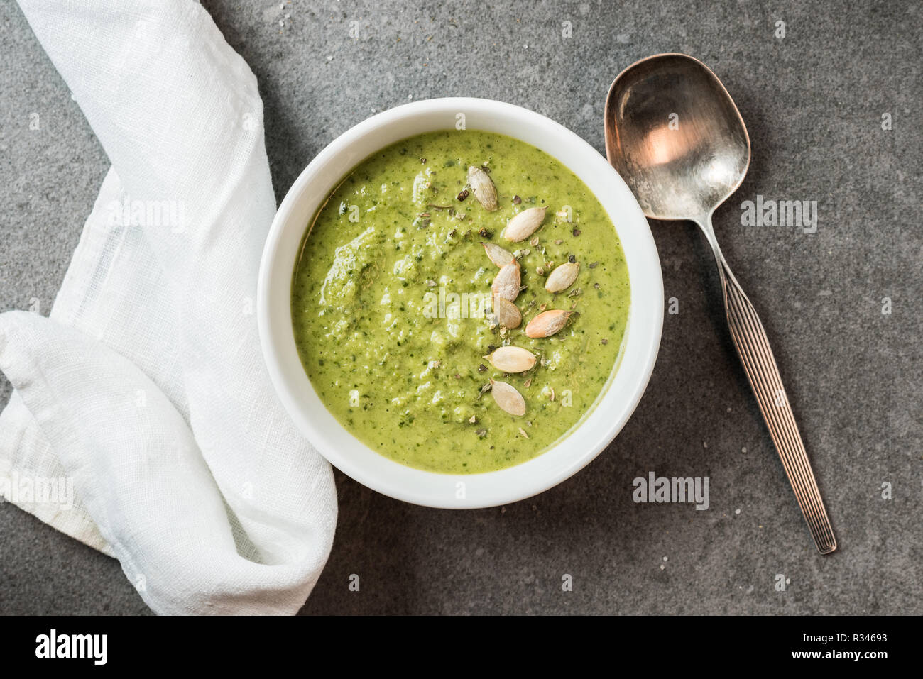 Top view of silver spoon, white cloth and homemade green creamy soup in bowl Stock Photo