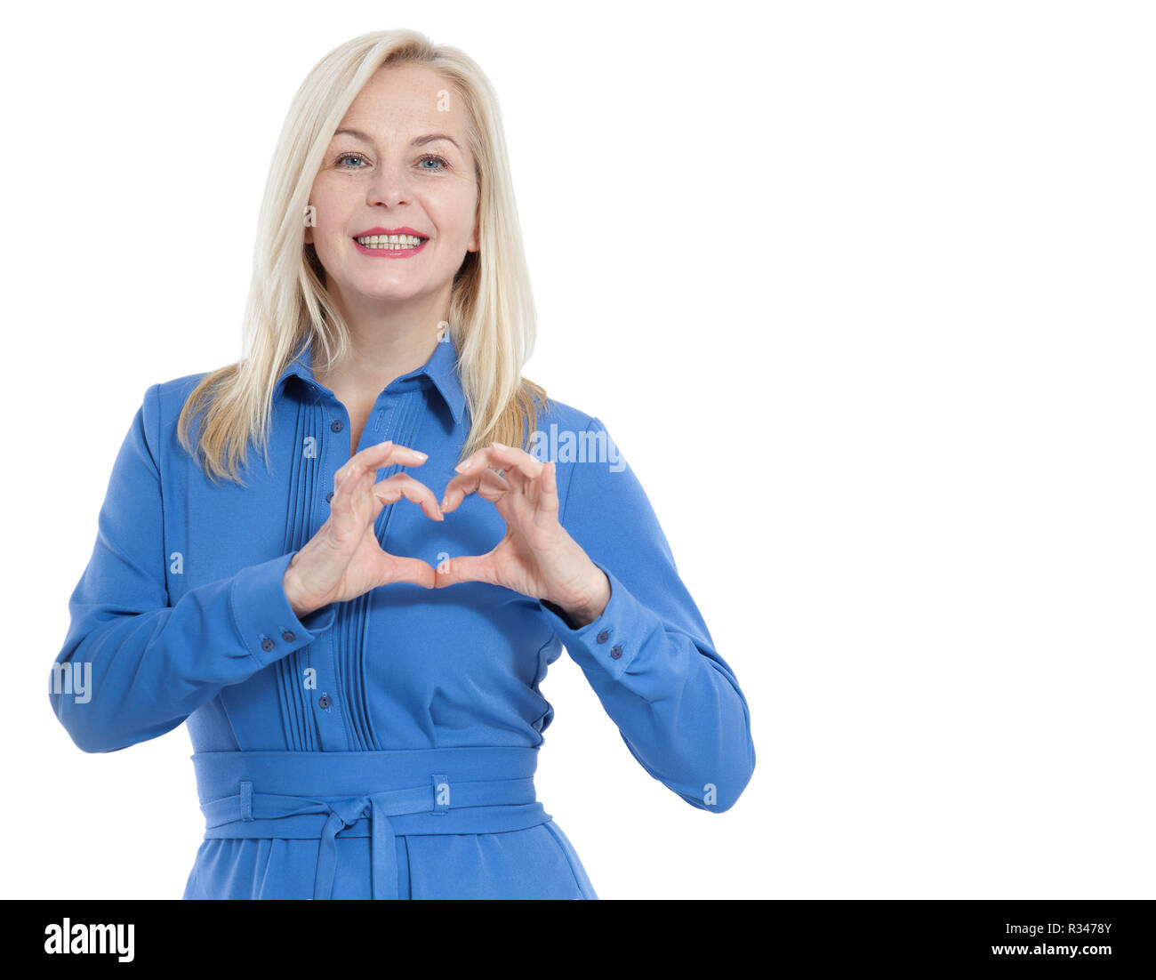 Friendly smiling middle aged woman in blue dress looks at the camera and shows a gesture I love you isolated on white background. Stock Photo