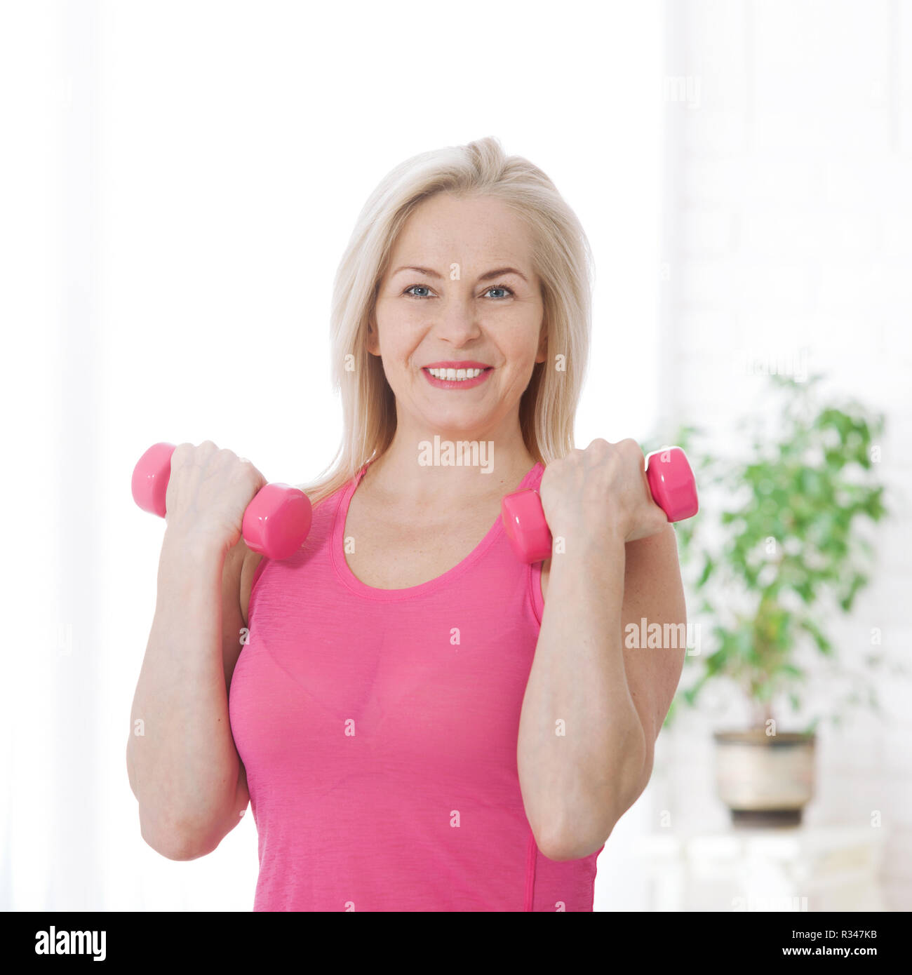 Happy middle aged woman lifting dumbbells at home in living room. Fitness concept. Stock Photo