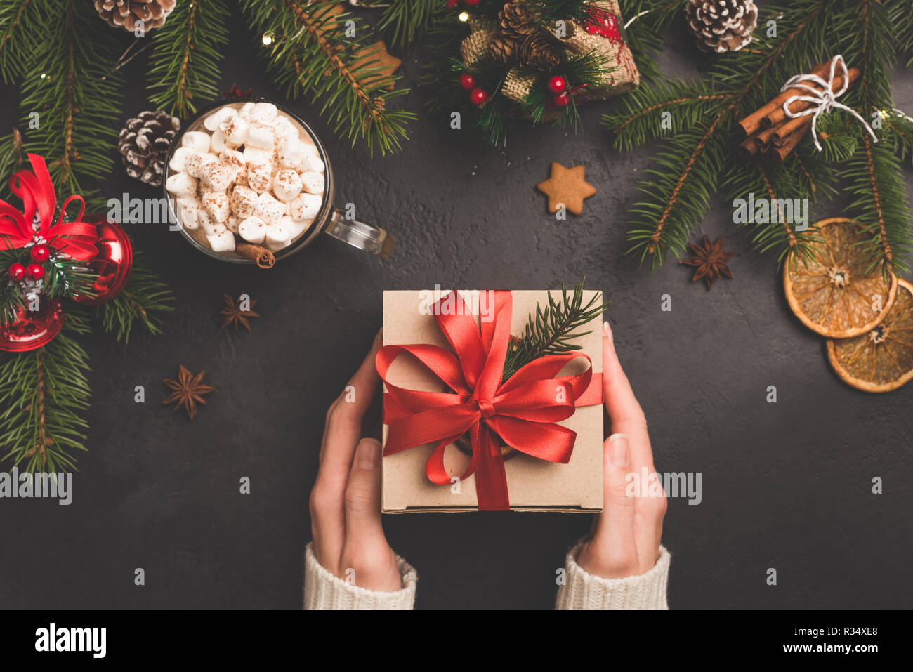 Christmas gift box in craft paper with red ribbon. Winter holidays New Year or Christmas background flat lay composition, person holding gift box Stock Photo