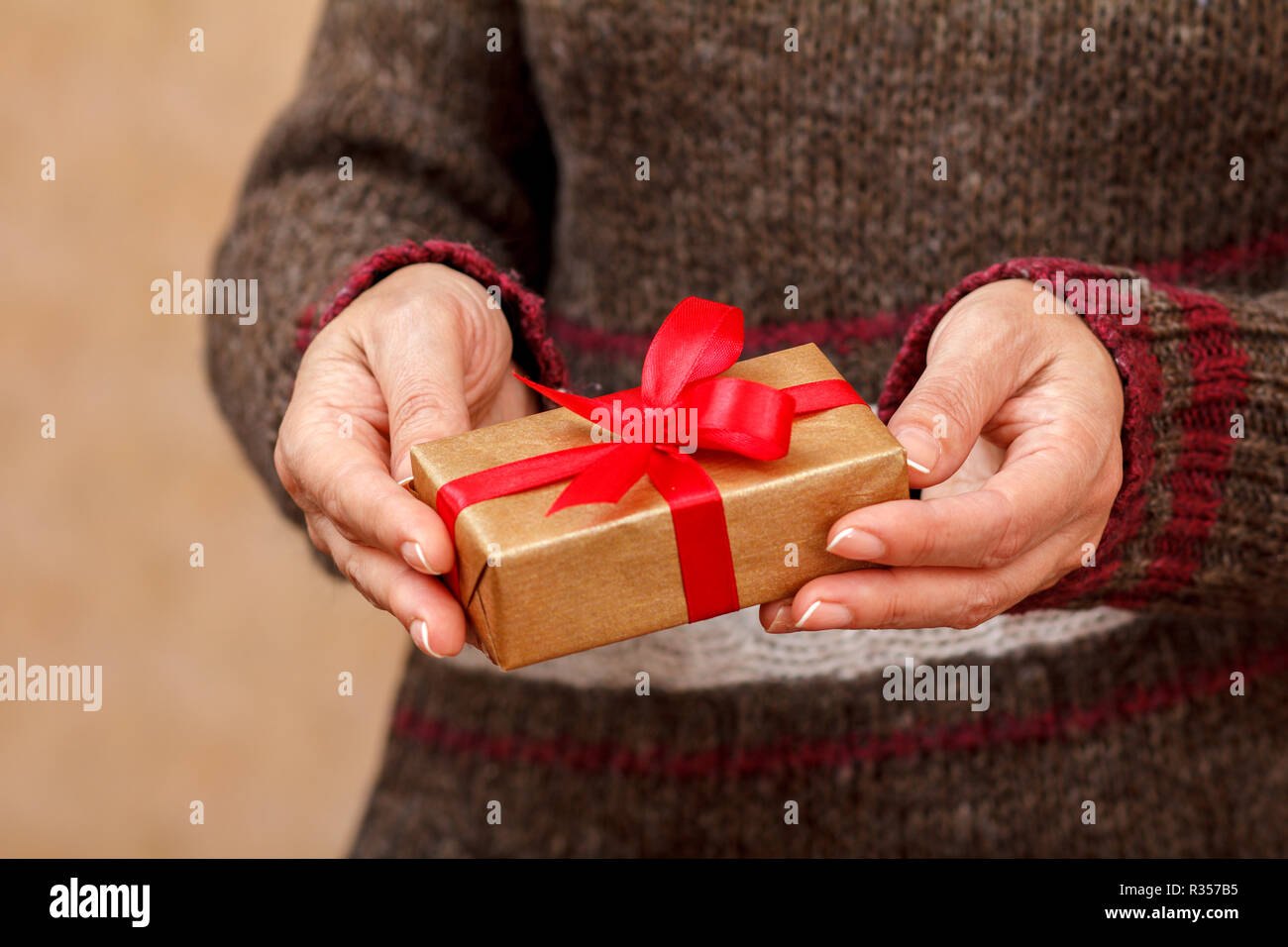 Woman in a sweater holding a gift box tied with a red ribbon in her hands. Shallow depth of field, Selective focus on the box. Concept of giving a gif Stock Photo
