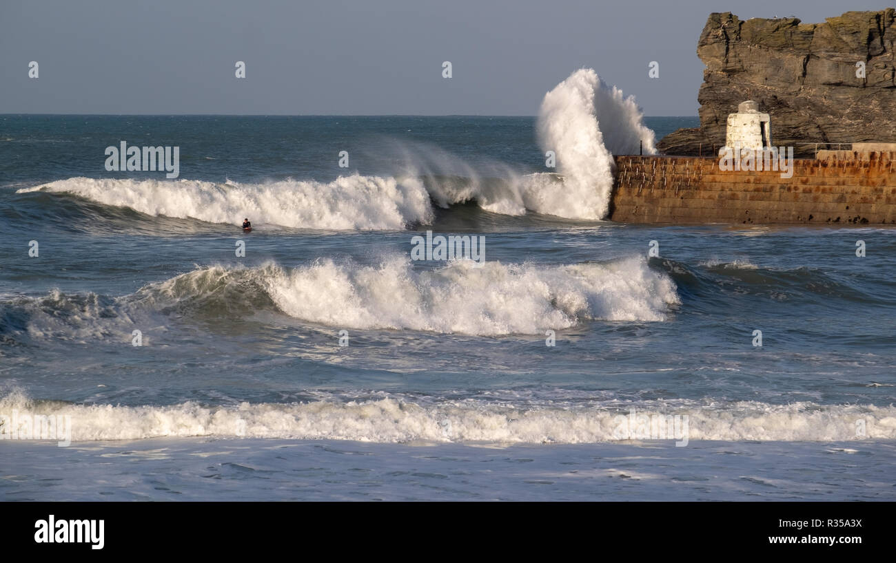 Single surfer almost lost in the crashing waves at Portreath harbour in the wind and sunshine as the waves break over the harbour wall. Stock Photo
