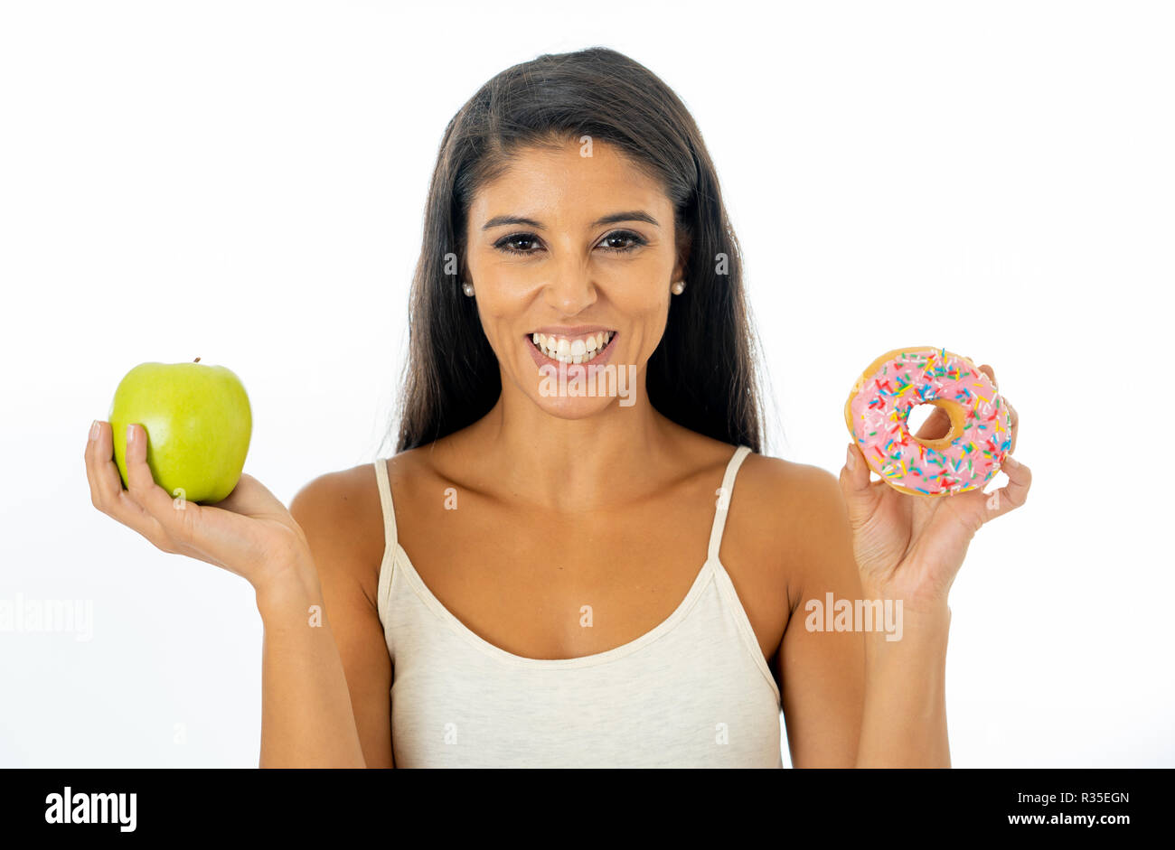 Beautiful happy young woman having to make choice between apple and doughnut in healthy unhealthy food, detox eating, calories and diet concept. Stock Photo
