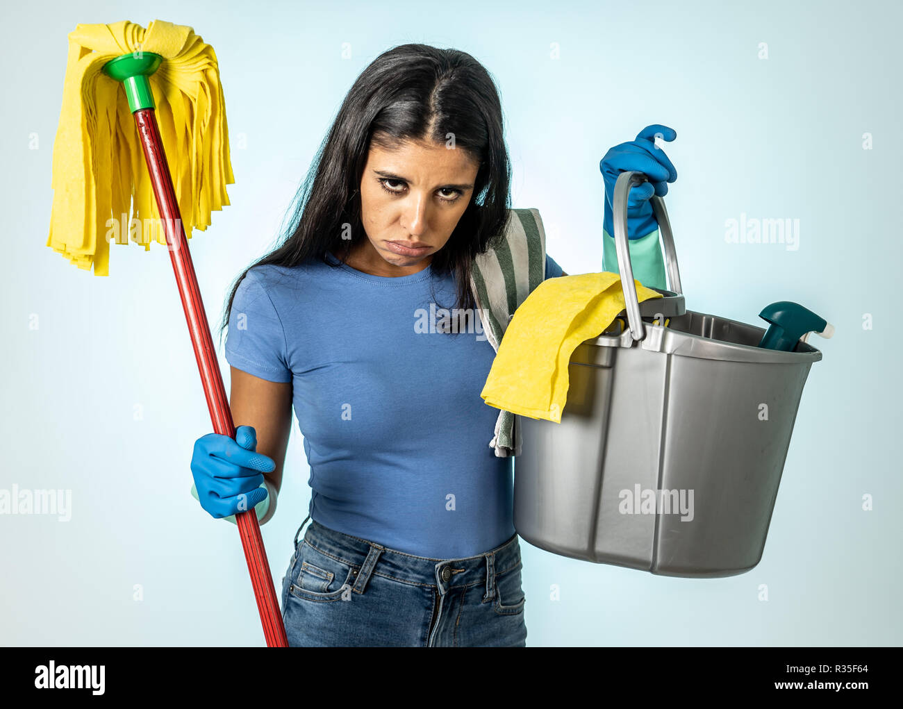 Young beautiful angry and upset housewife woman holding bucket mop