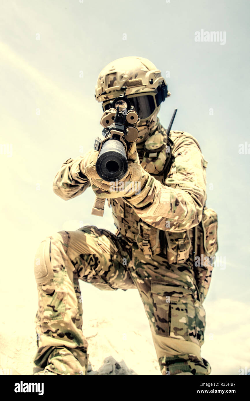 Airsoft war game player in army combat camouflage uniform, protected with helmet and tactical glasses, aiming in camera with optical sight on service  Stock Photo