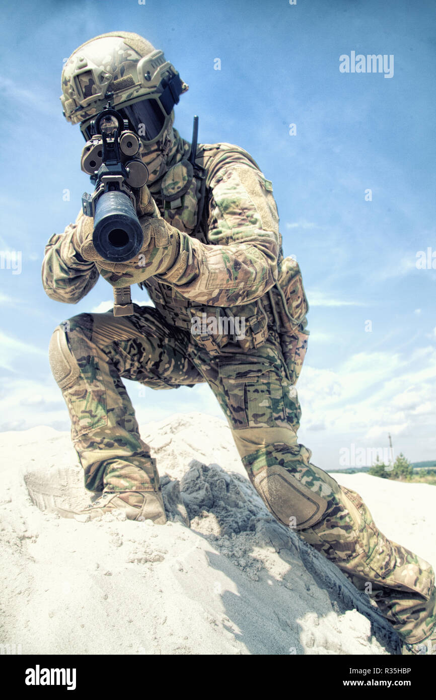 Airsoft war game player in army combat camouflage uniform, protected with helmet and tactical glasses, aiming in camera with optical sight on service  Stock Photo