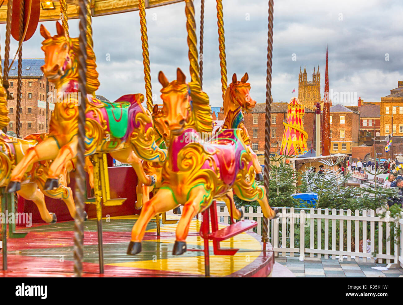 Merry go round carousel fairground ride at Gloucester Quays Victorian Christmas Market with tower of Gloucester Cathedral, Gloucester. hdr effect Stock Photo