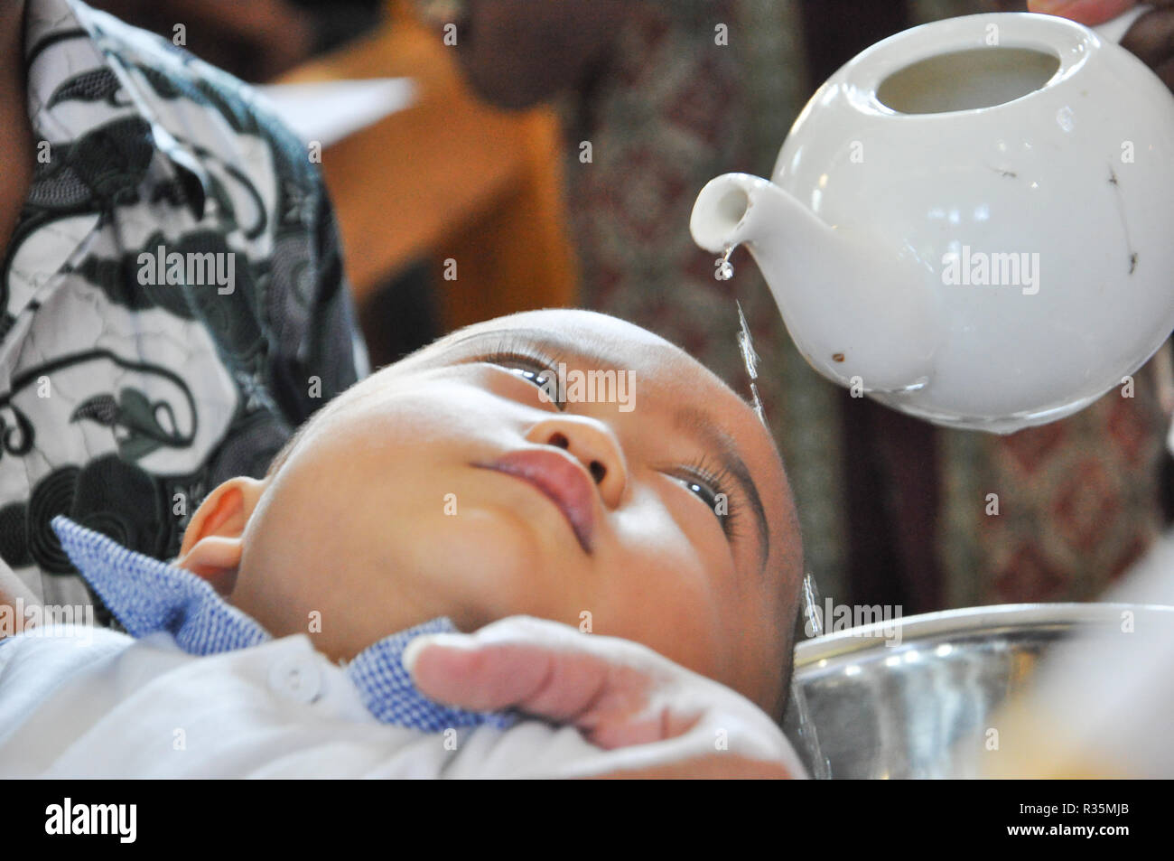 Batam, Indonesia. A priest pours water on the head of a chils during baptism procession. Stock Photo