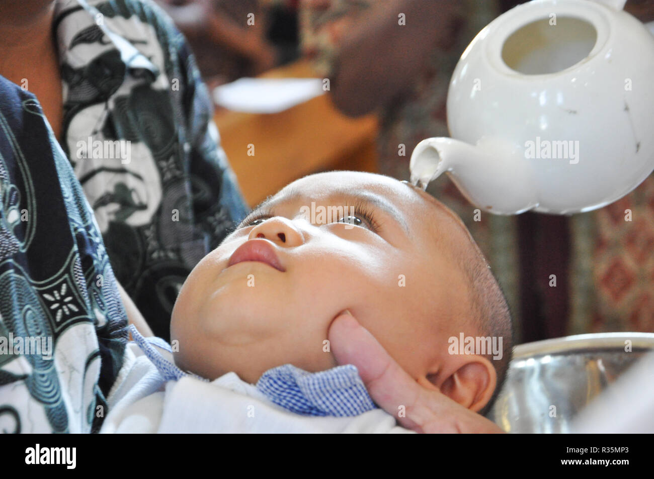 Batam, Indonesia. A priest pours water on the head of a chils during baptism procession. Stock Photo