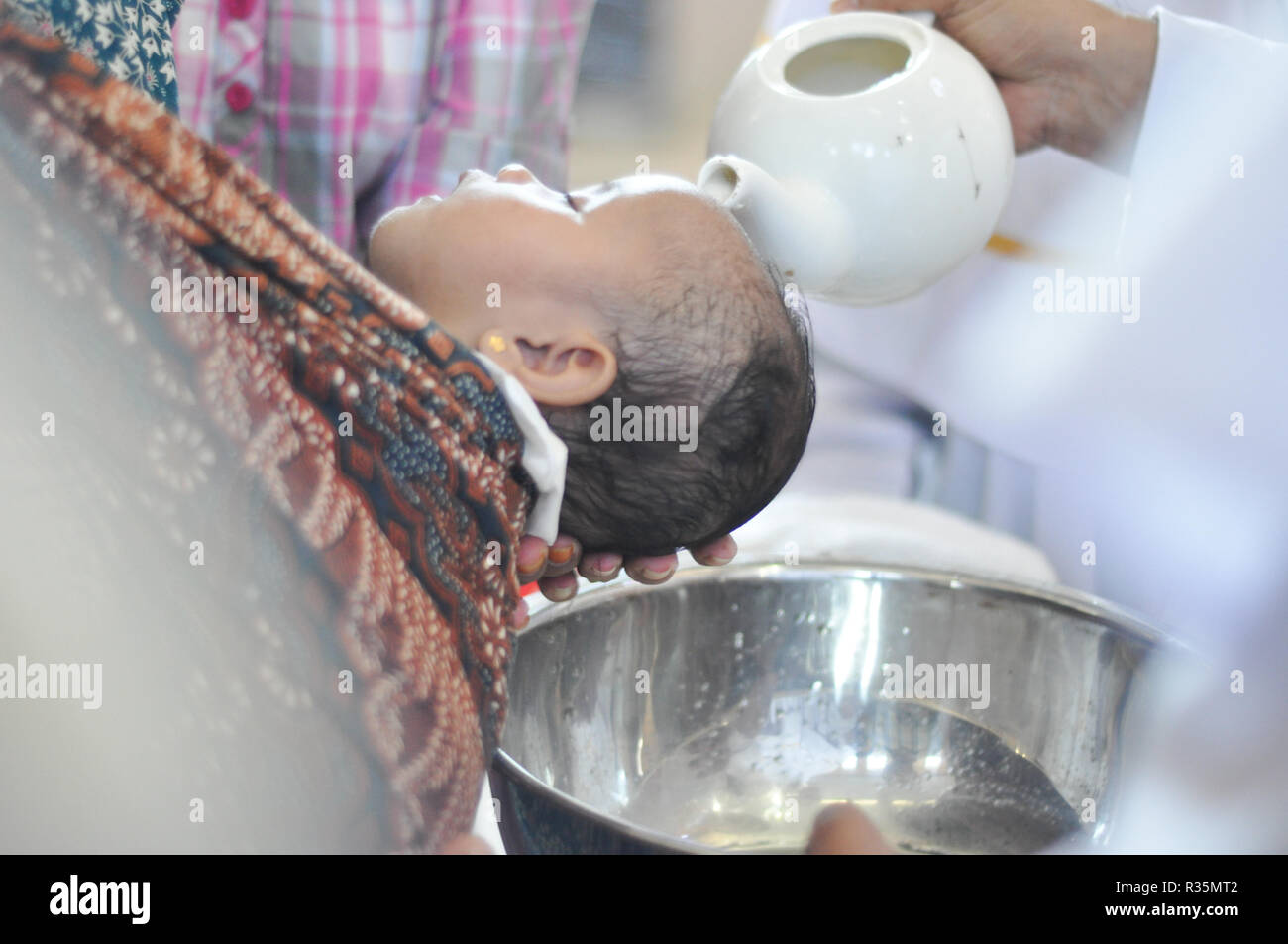 Batam, Indonesia. A priest pours water on the head of a chils during baptism procession. Stock Photo