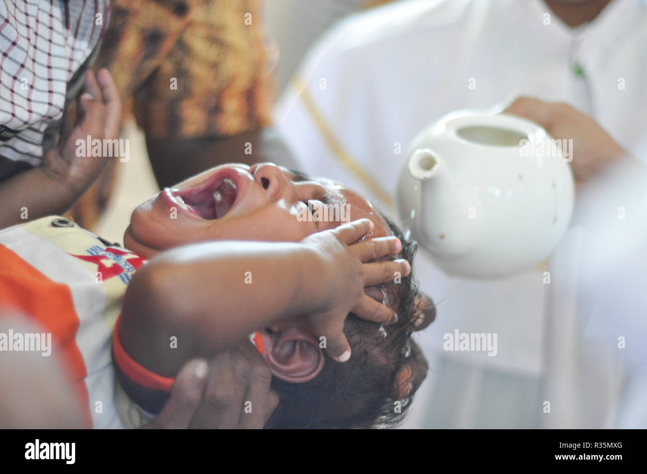 Batam, Indonesia. A priest pours water on the head of a chils during baptism procession. Stock Photo
