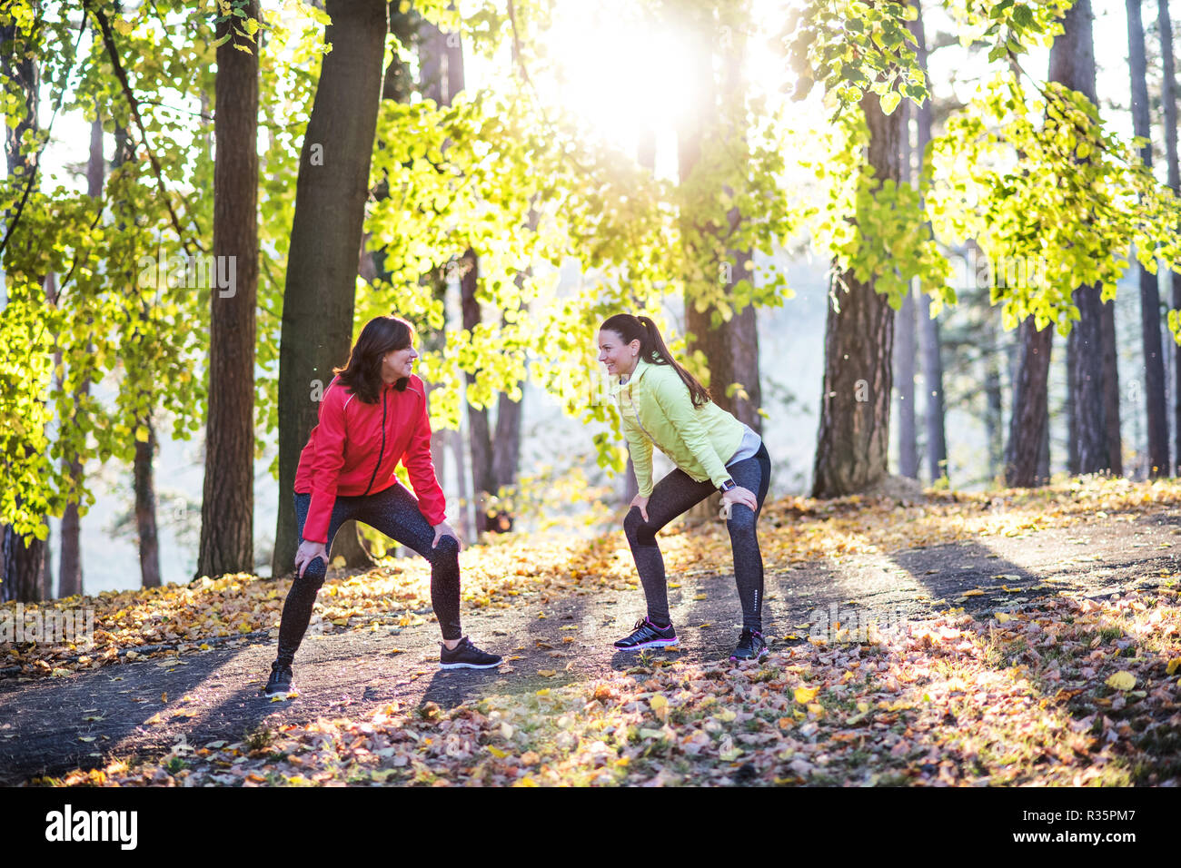 Two female runners stretching outdoors in forest in autumn nature. Stock Photo