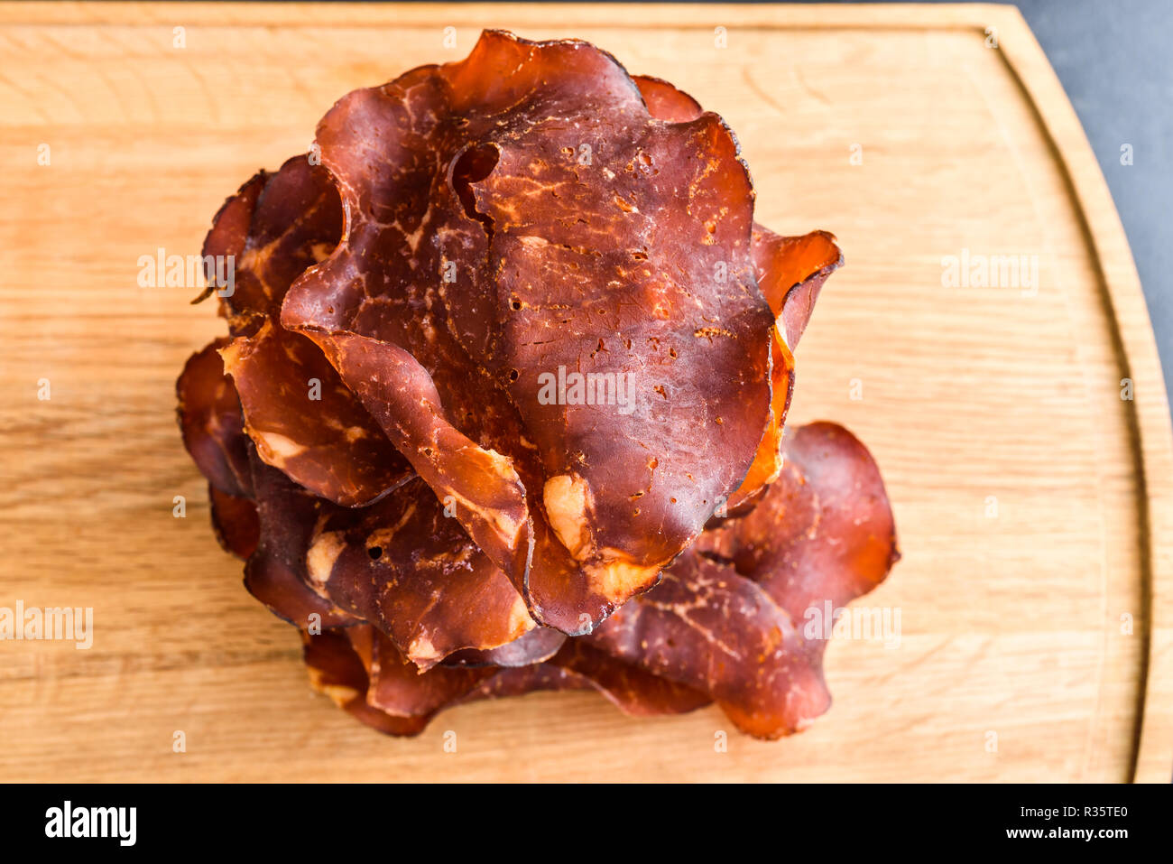 Thinly sliced and dried smoked ham on oak tray. Small crystals of salt visible on the meat. Stock Photo