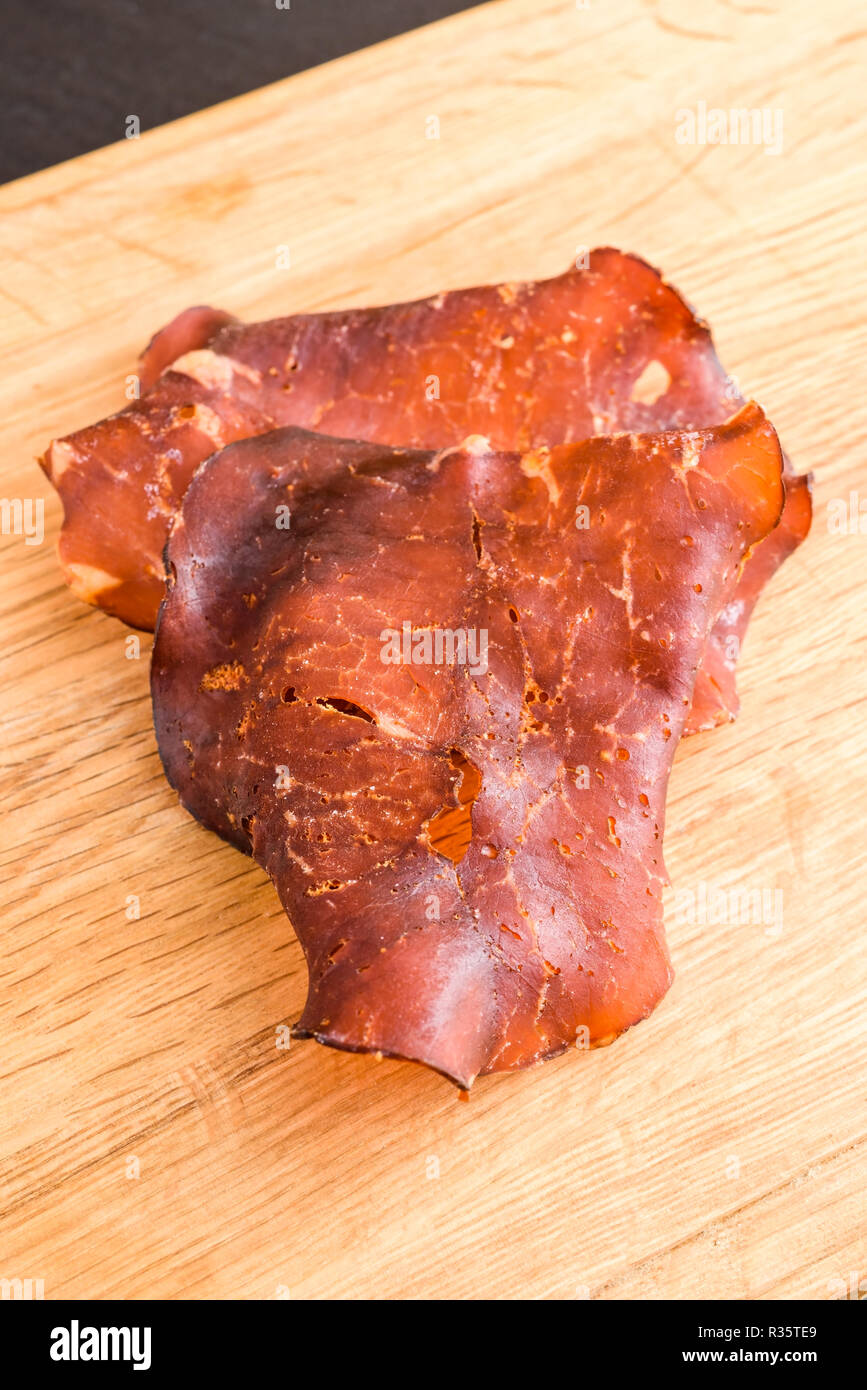 Thinly sliced and dried smoked ham on oak tray. Small crystals of salt visible on the meat. Stock Photo