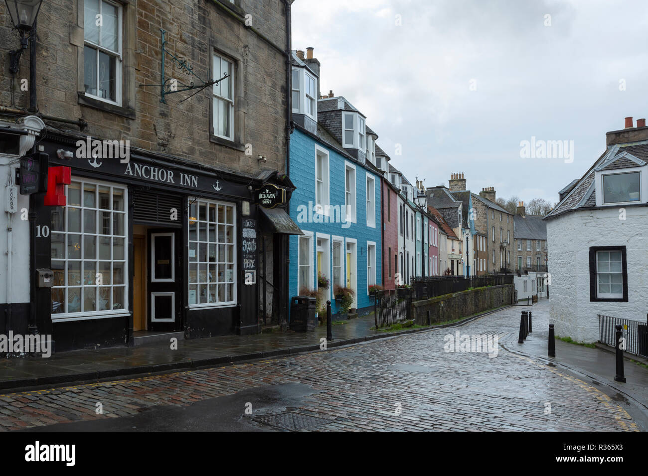 A pub and brightly coloured terraced houses along a cobbled street in South Queensferry, Edinburgh. On a wet day. Stock Photo