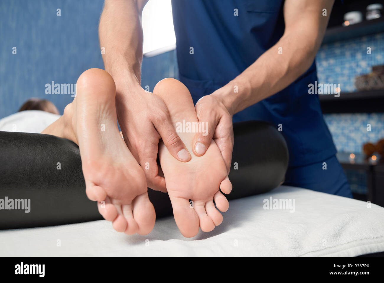 Closeup of hands of qualified masseur massaging foot of  female client in spa cosmetology salon. Woman lying on couch, relaxing and enjoying during healthy procedure. Concept of body care. Stock Photo