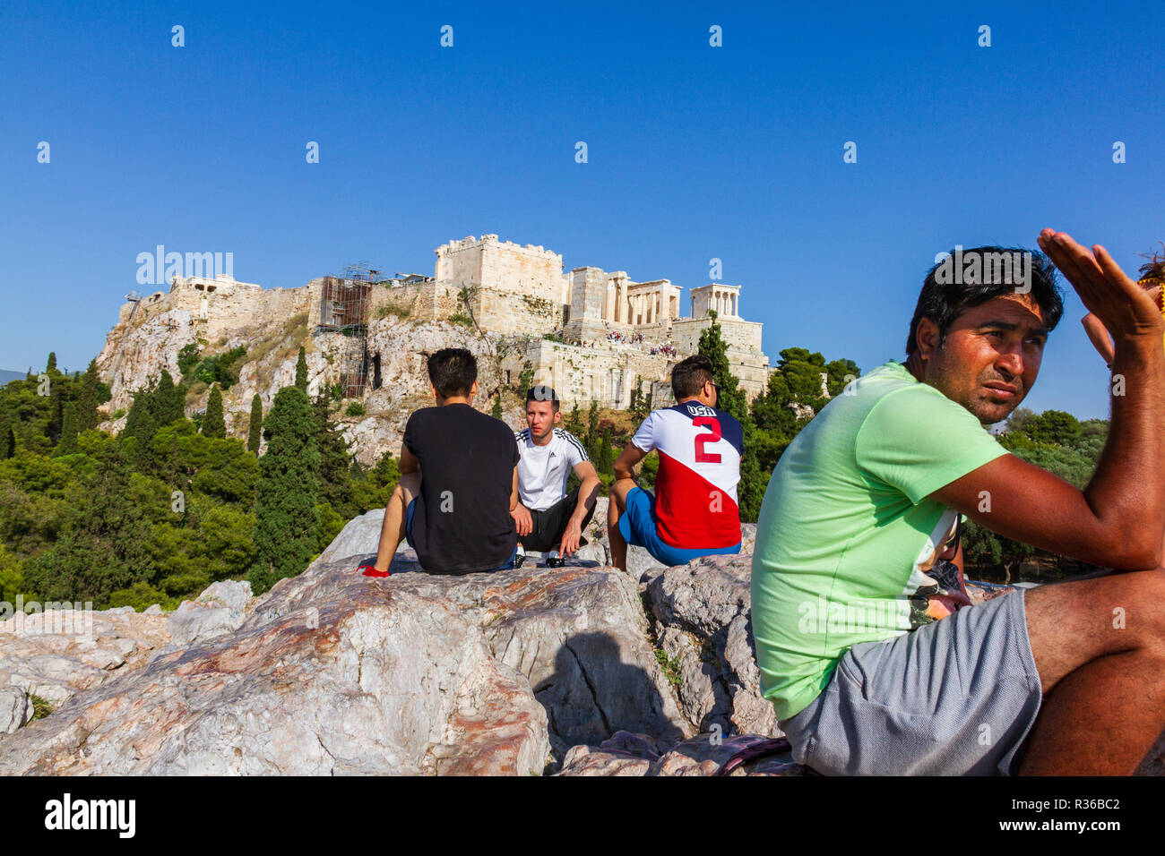 Athens, Greece - June 9, 2018: People seated on a rock and chatting against the Acropoilis ruins in Athens, Greece on a summer afternoon Stock Photo