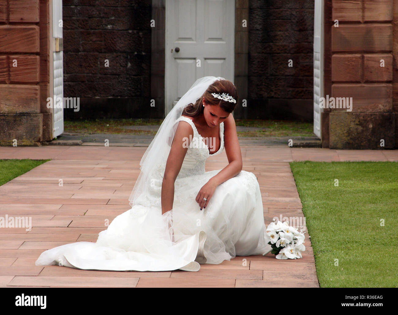 A bride, at her wedding venue, kneels down to sort her dress in preparation for the ceremony in Scotland. Stock Photo