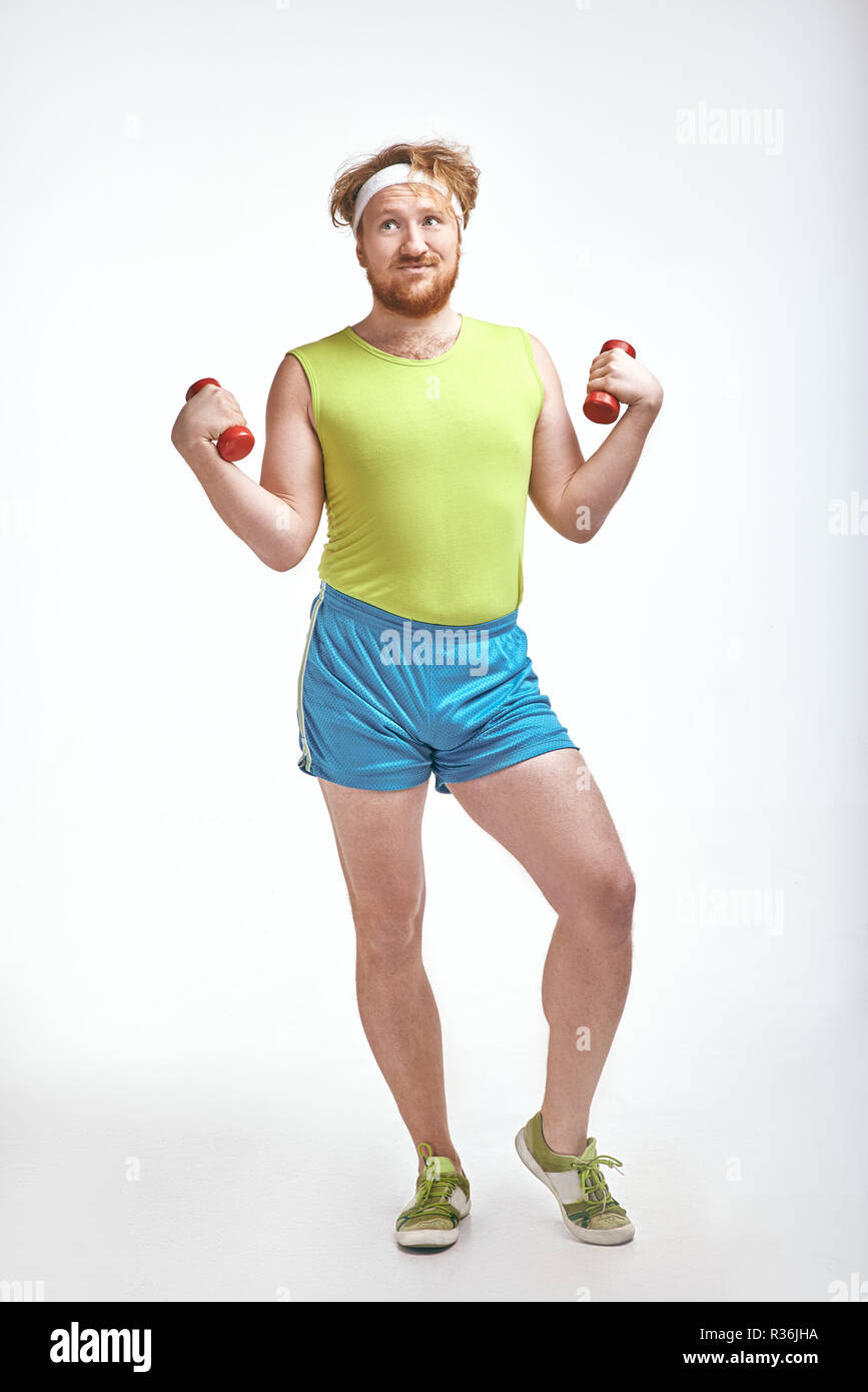 Red haired, bearded, plump man is holding the dumbbells Stock Photo