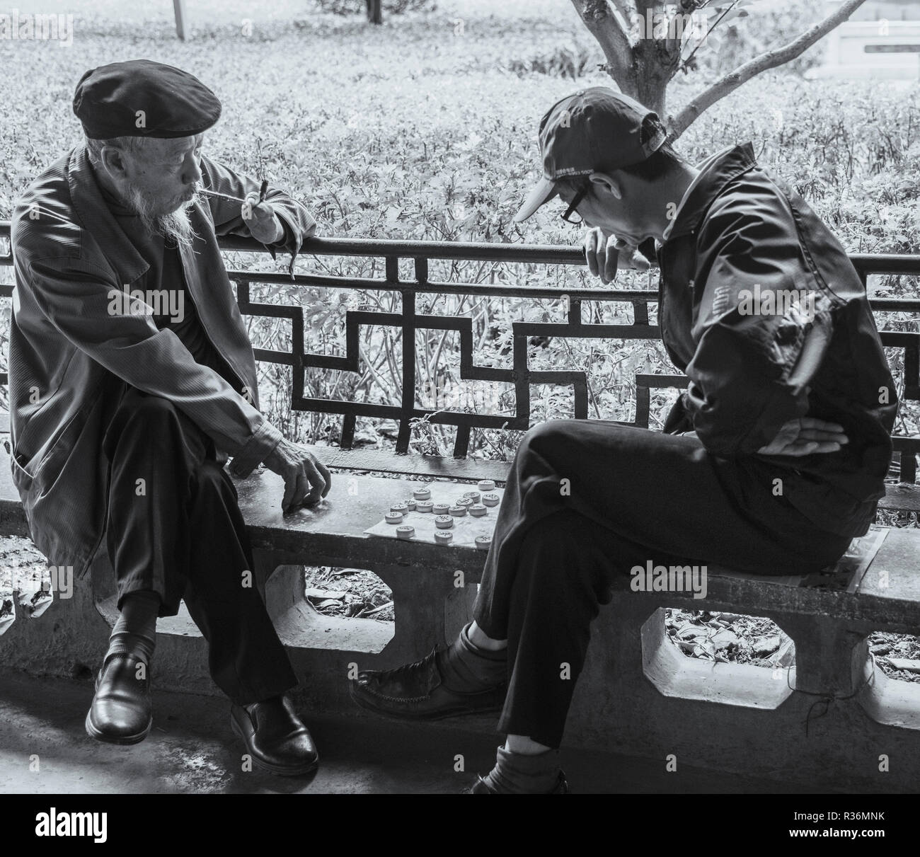 Black and white photo of two elderly chinese gentlemen playing popular game of mah jong in chinese park kunming china