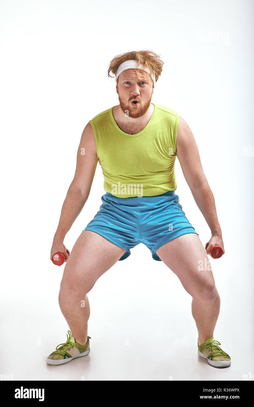 Red haired, bearded, plump man is holding the dumbbells Stock Photo