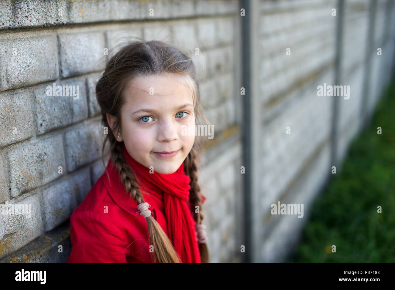 girl in red raincoat near concrete fence outdoor Stock Photo