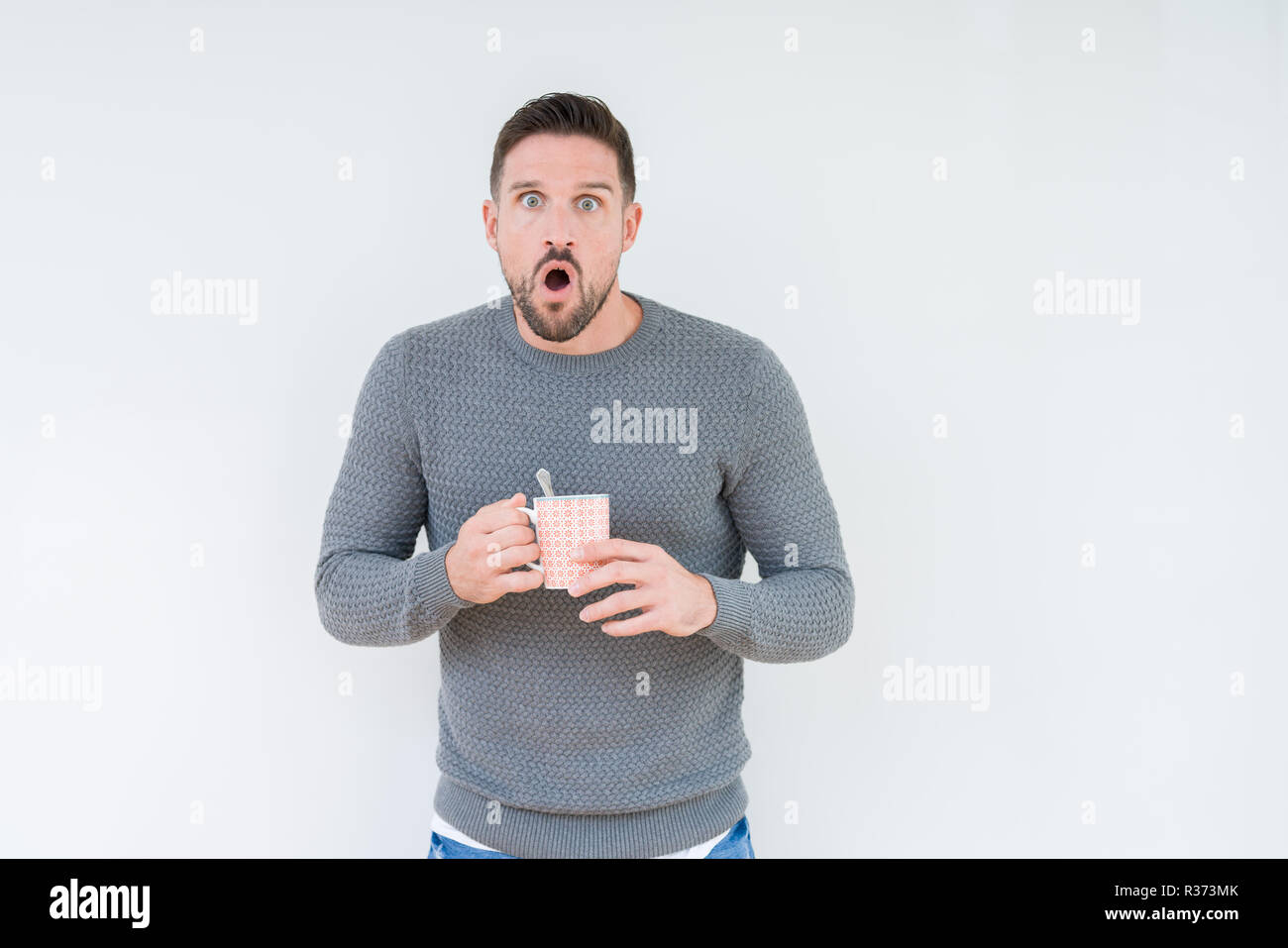 Young man driking cup of coffee over isolated background scared in