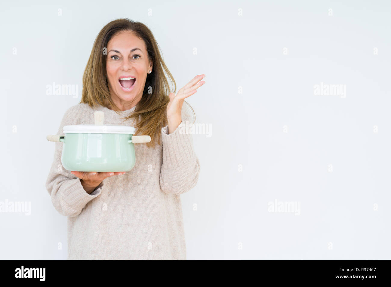 Middle age housewife woman holding iron cooking pot over isolated background very happy and excited, winner expression celebrating victory screaming w Stock Photo